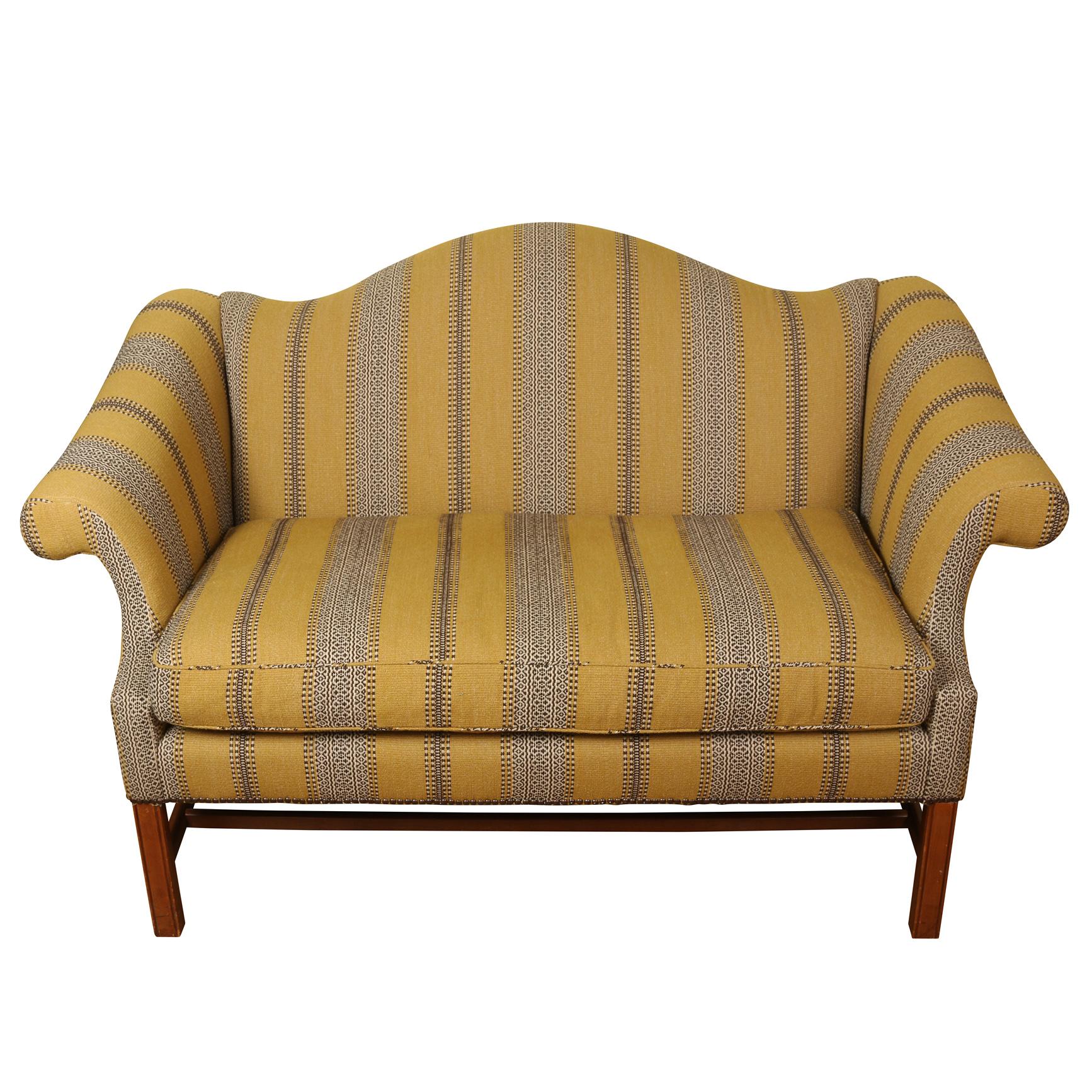 A  handsome Georgian style camelback settee with a flat back, loose seat cushion and rolled arms, on squared mahogany legs.  The upholstery, a woven stripe, is in excellent condition.