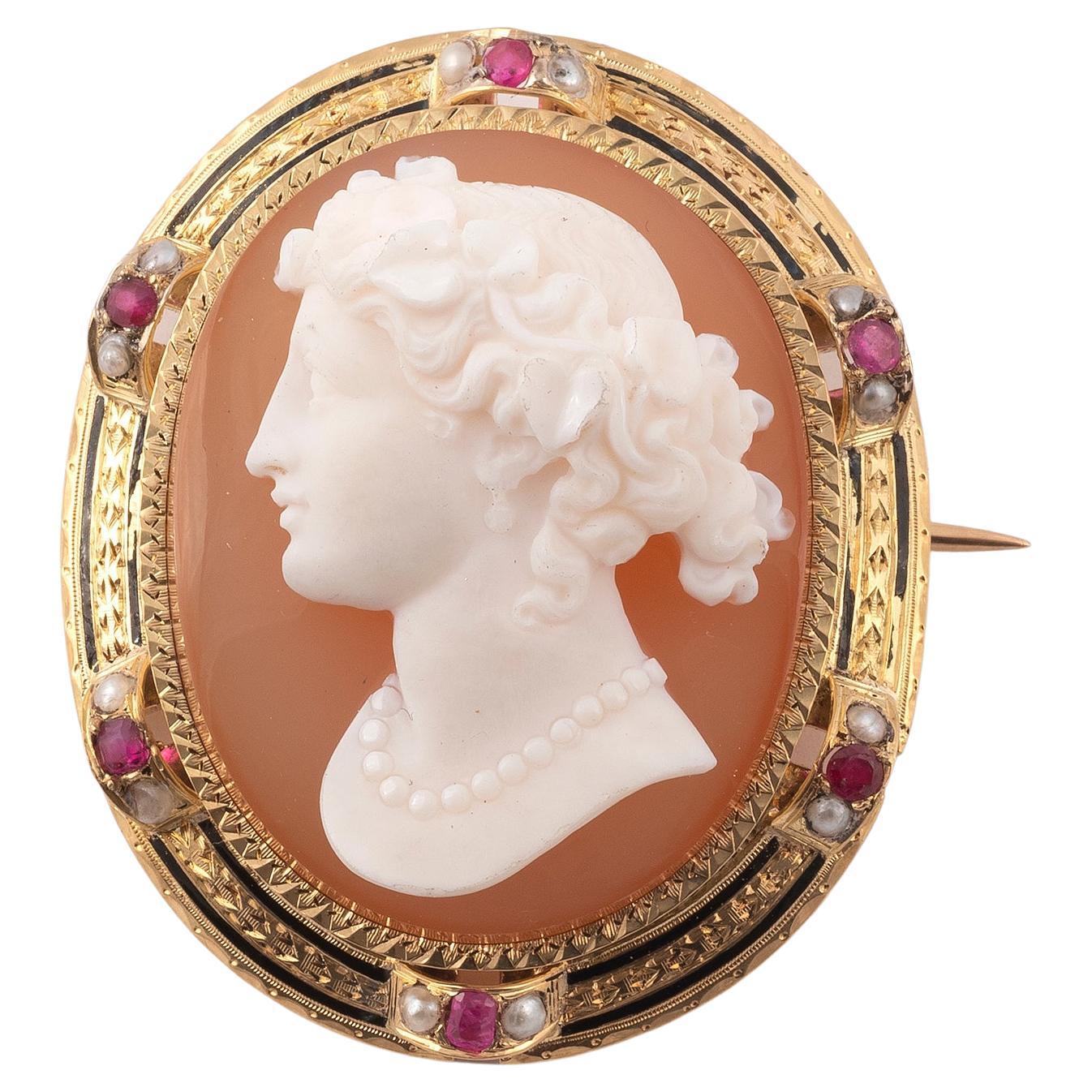 Brooch with a cameo on agate in an oval decoration punctuated with rubies, white pearls and black enamel. 18K yellow gold frame. French work. Original box. Dimensions: 4.5 x 3.80 cm.  Weight: 26.56 g.