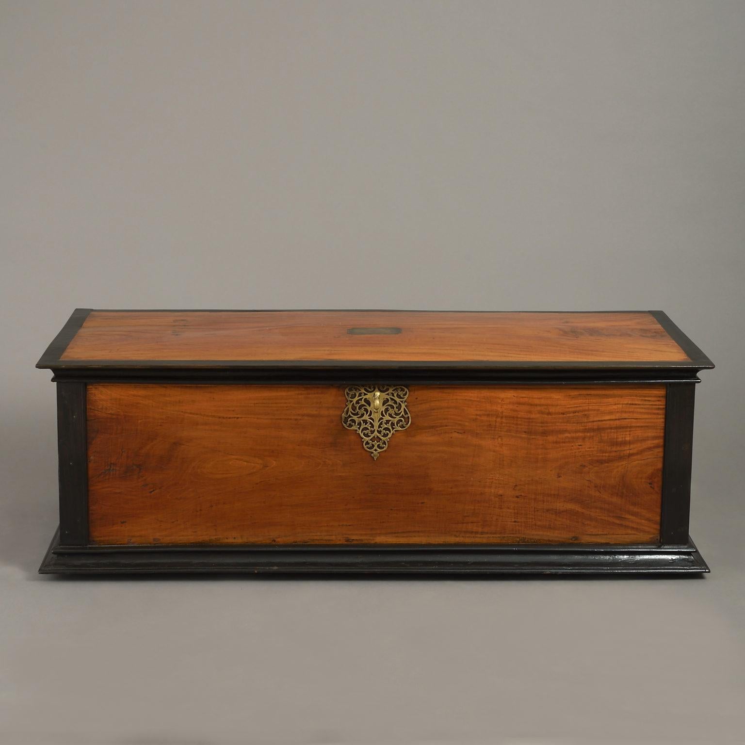 A finely figured camphor wood trunk of rectangular form, the top, corners and base mounted with ebony, having intricate brass carrying handles at either end and a central lock escutcheon and key of the same. The top opens to reveal a candle box.