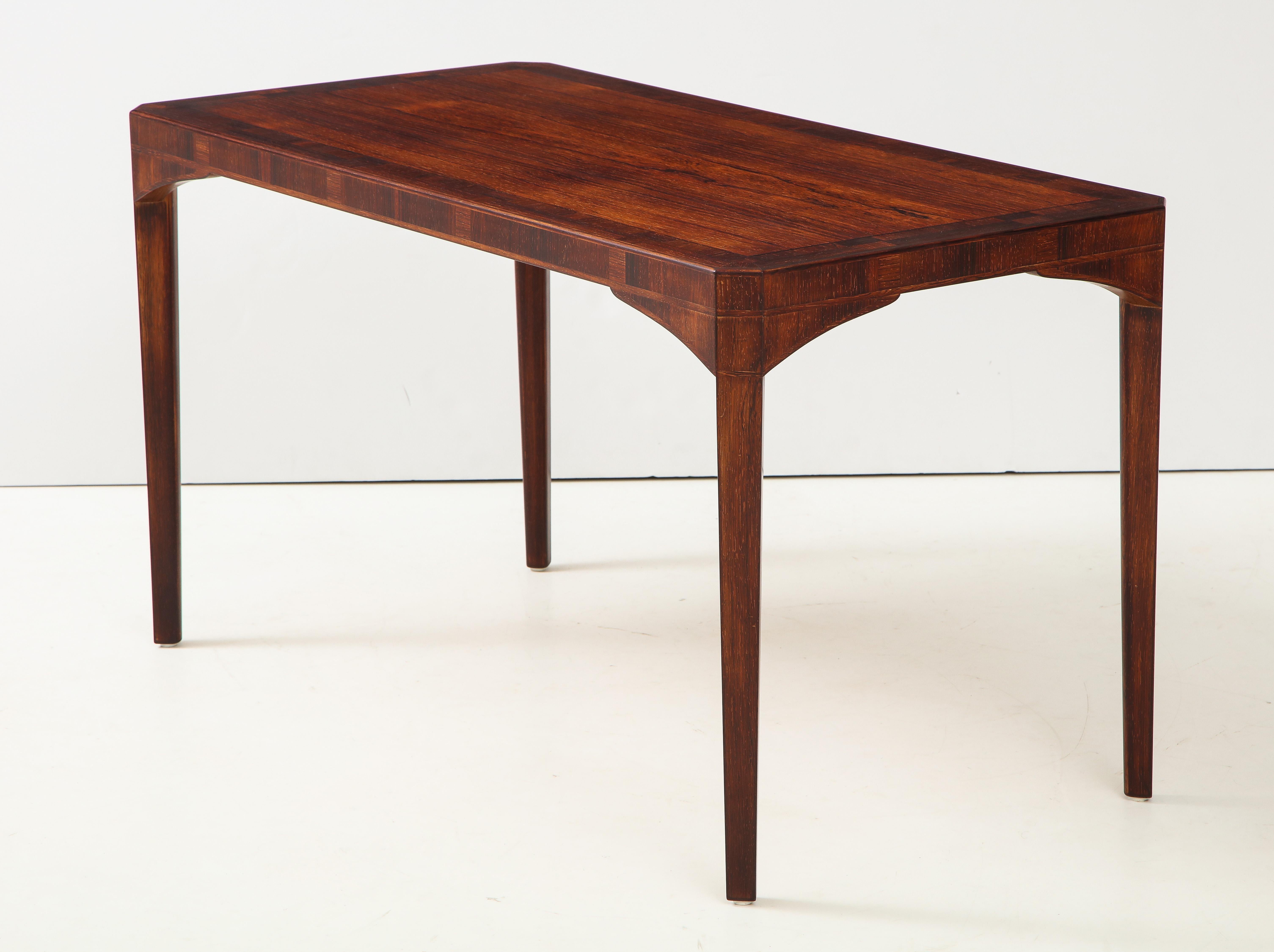 A Swedish rosewood table designed by Carl Malmsten, Stamped on verso with owners name and year, circa 1967. With a rectangular top, geometric inlays and canted corners.