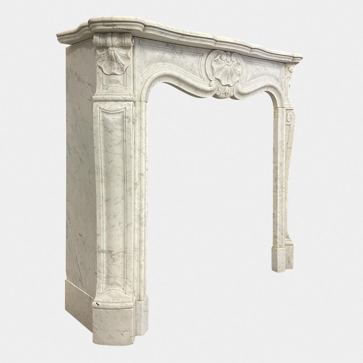 A compact Carrara marble antique Louis XV fireplace with serpentine shelf and frieze. Scrolled and panelled cabriole jambs, surmounted by carved shell corner blocks with conforming centre cartouche. 

Circa 1850 

opening size 
88cm H X 74cm W.