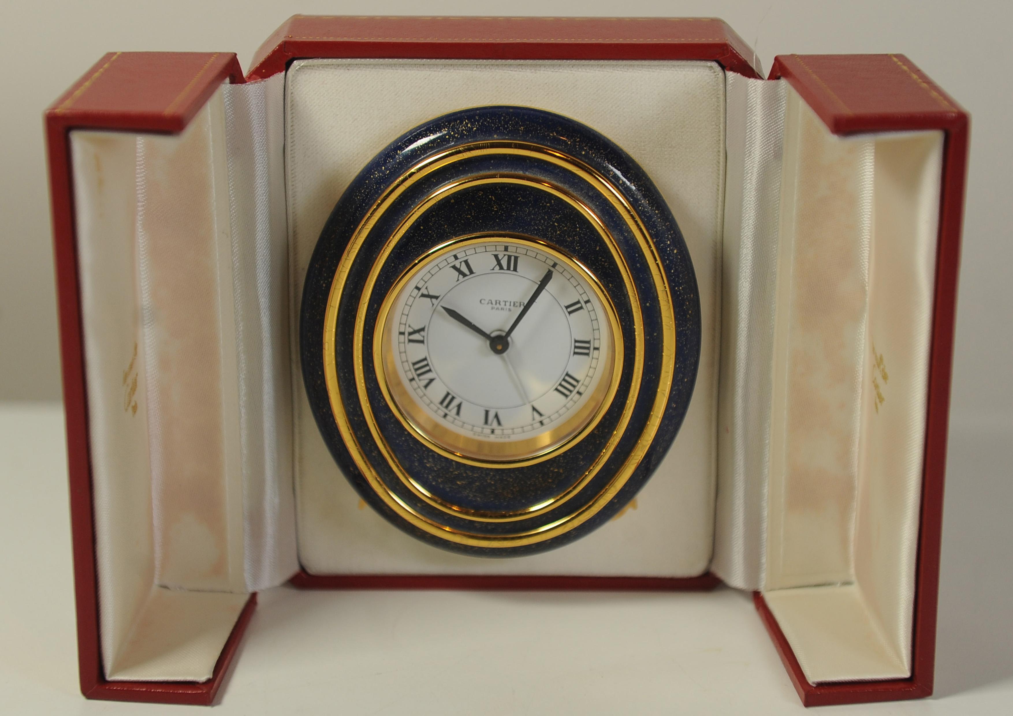 An Elegant Cartier Gold & Blue Circular 8-Day Mechanical Movement Oval Desk Clock of Gilt Metal and Blue Enamel With White Dial & Roman Numerals 

Supplied With A Red Box. 

Clock Is Made in Switzerland. 

Clock dimensions
Height 10.2cm
Width
