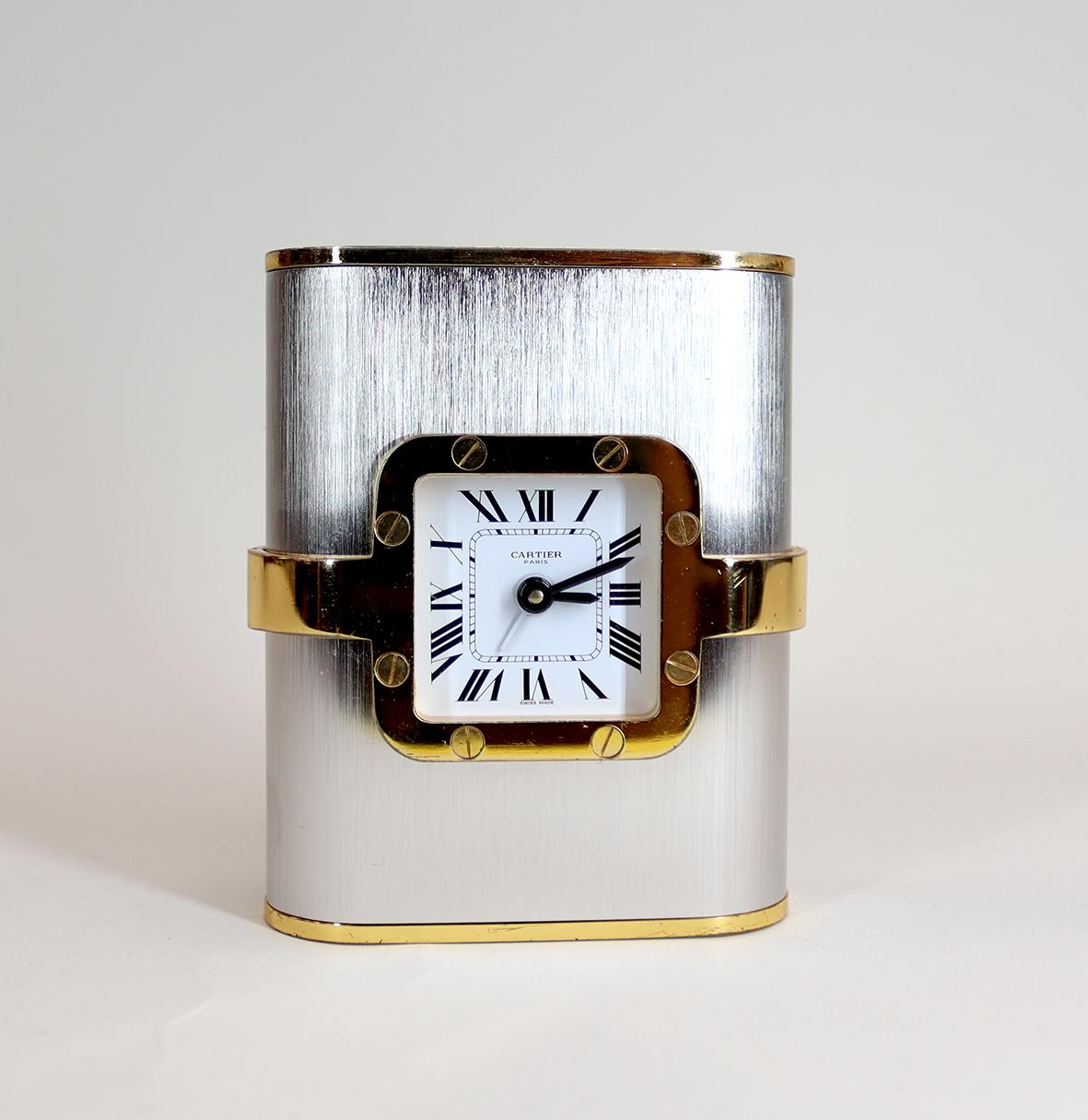 Une horloge de bureau Cartier dans le style de l'emblématique montre Santos de Cartier. Avec une lunette en or, un boîtier en acier brossé et des détails en dold.

Cette horloge est une horloge de bureau élégante et de haute qualité, fabriquée dans