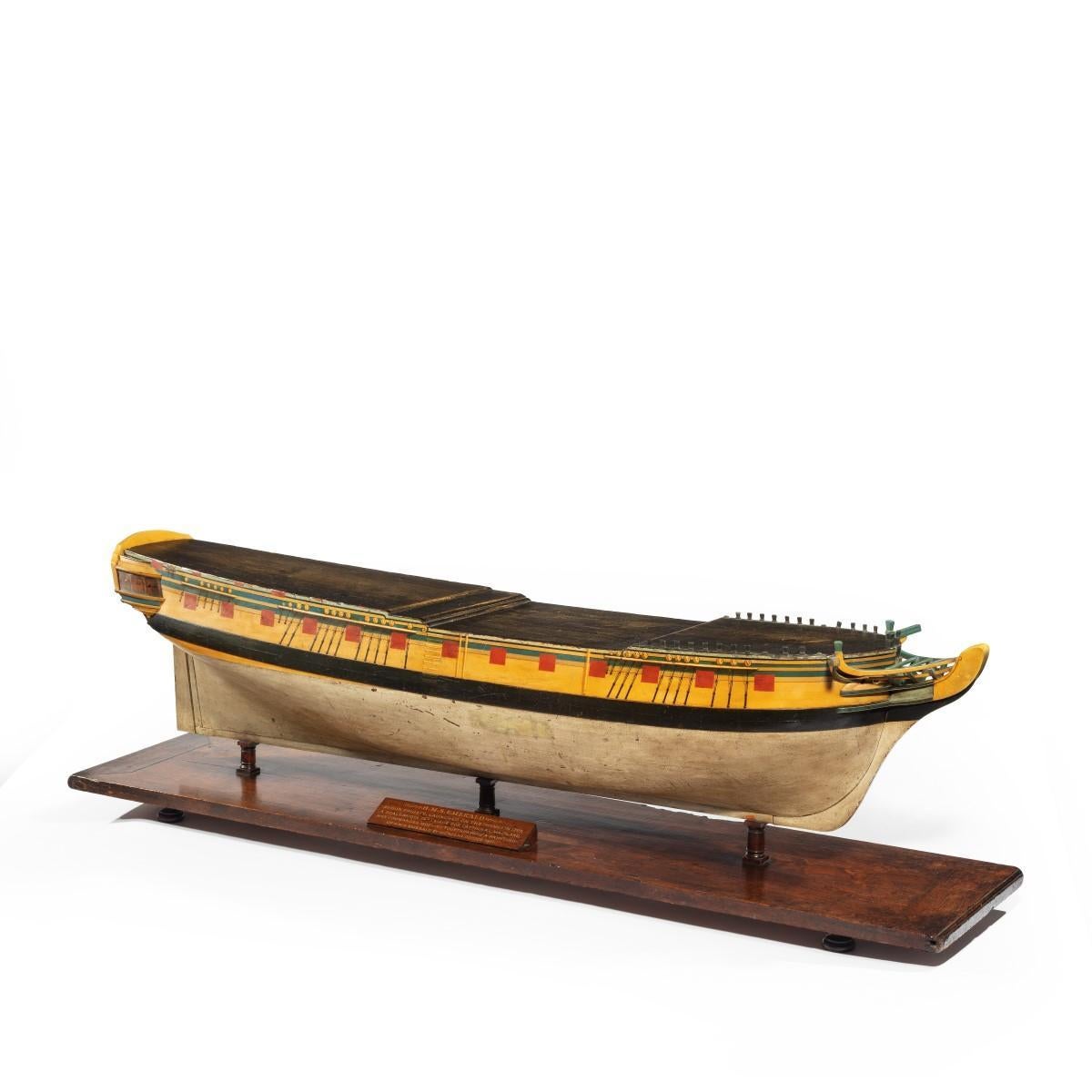 A carved and painted model of HMS Emerald, 1811, the frigate finely modelled and painted with a white hull, black plimsole line, yellow topsides and red cannon ports, raised on the original mahogany stand with turned feet and a plaque reading