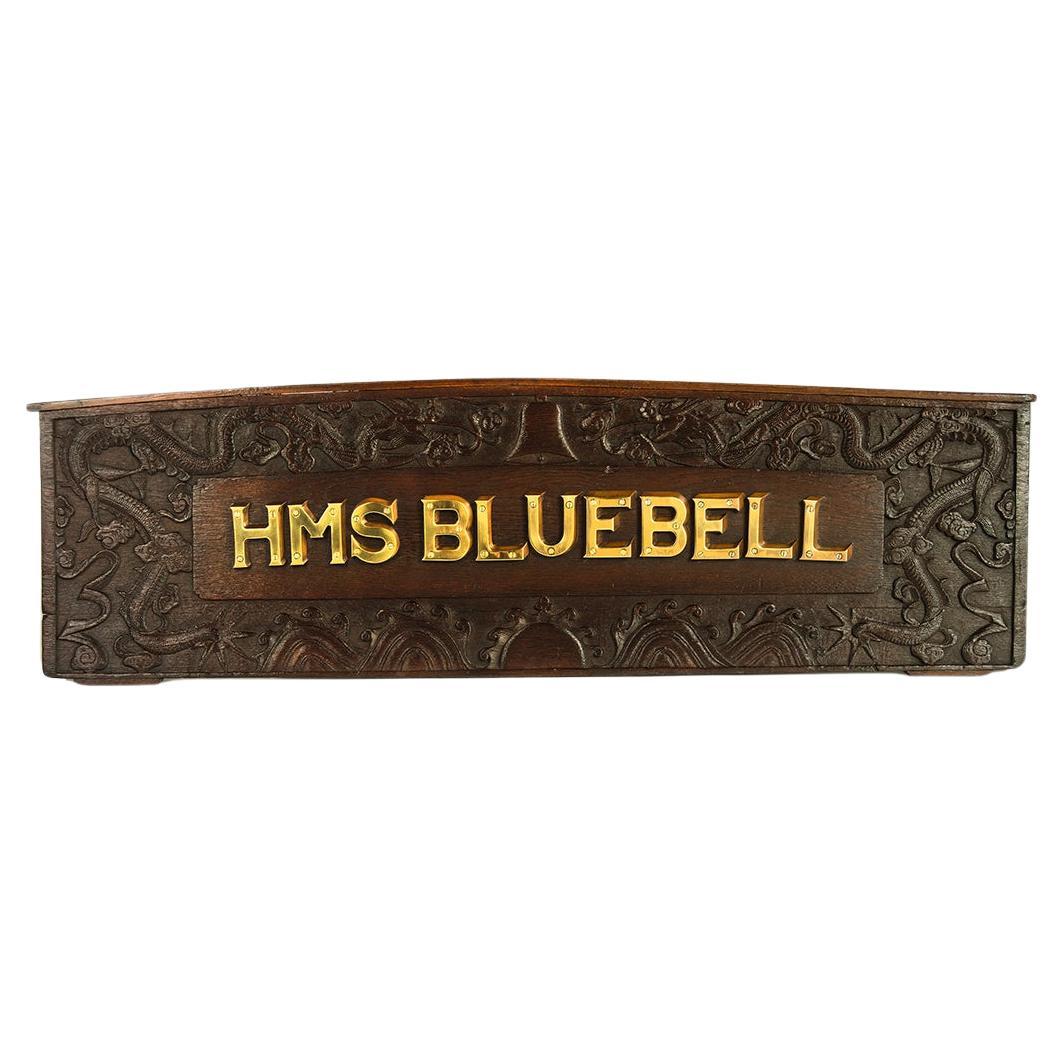 A carved and shaped teak seat back from the launch of minesweeper H M S Bluebell, of shaped rectangular form with a central panel with 3in brass lettering HMS Bluebell, with braced back supports, carved with a confronting pair of sinuous dragons on