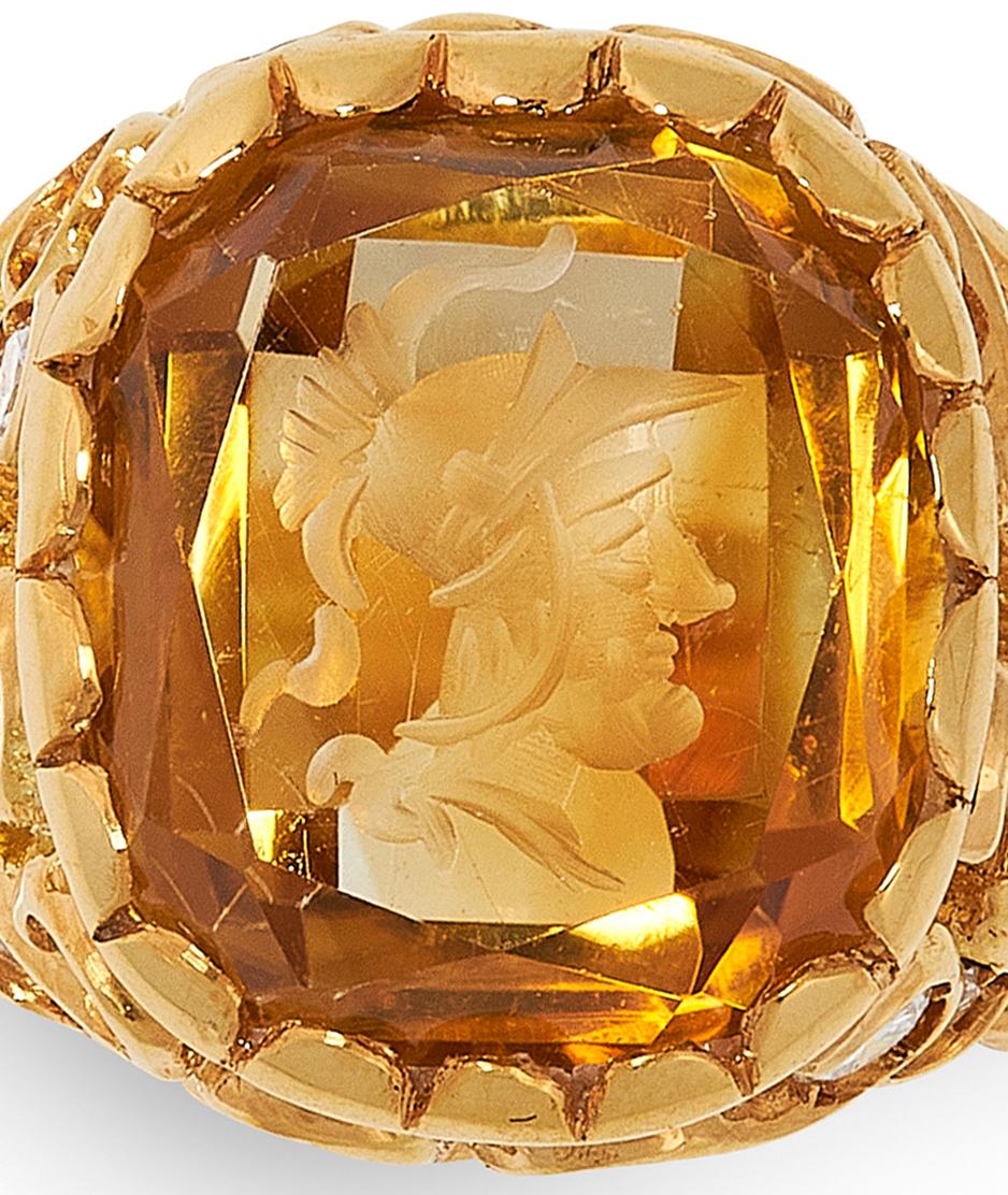 An Intricately carved citrine intaglio and diamond ring, set with a cushion shaped citrine with a carved depiction of a centurion to the front. The citrine is within a scrolling openwork yellow gold mount set with round cut diamonds. The ring has