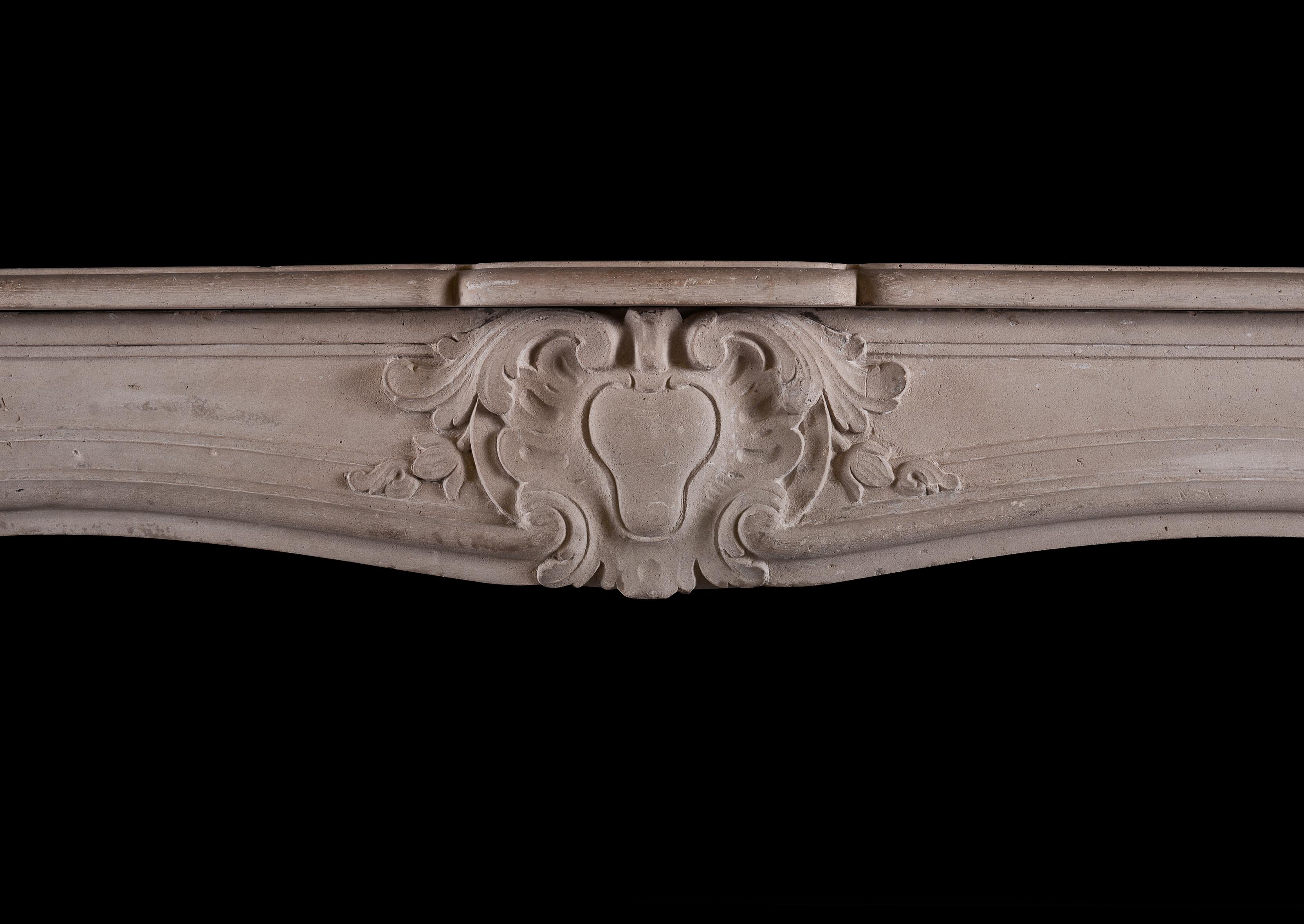 A carved French limestone fireplace in the Louis XV manner. The shaped, panelled jambs surmounted by shaped frieze with carved cartouche to centre flanked by scrolled foliage. Shaped shelf above. French, 19th century.

Measures: Shelf width: 1457 mm