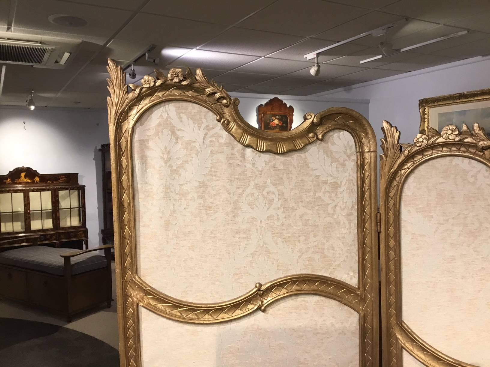 A carved giltwood French three fold vanity screen. Having a carved wooden frame which is gilded and houses shaped panels upholstered in a patterned silk, French, circa 1900

Dimensions: 68