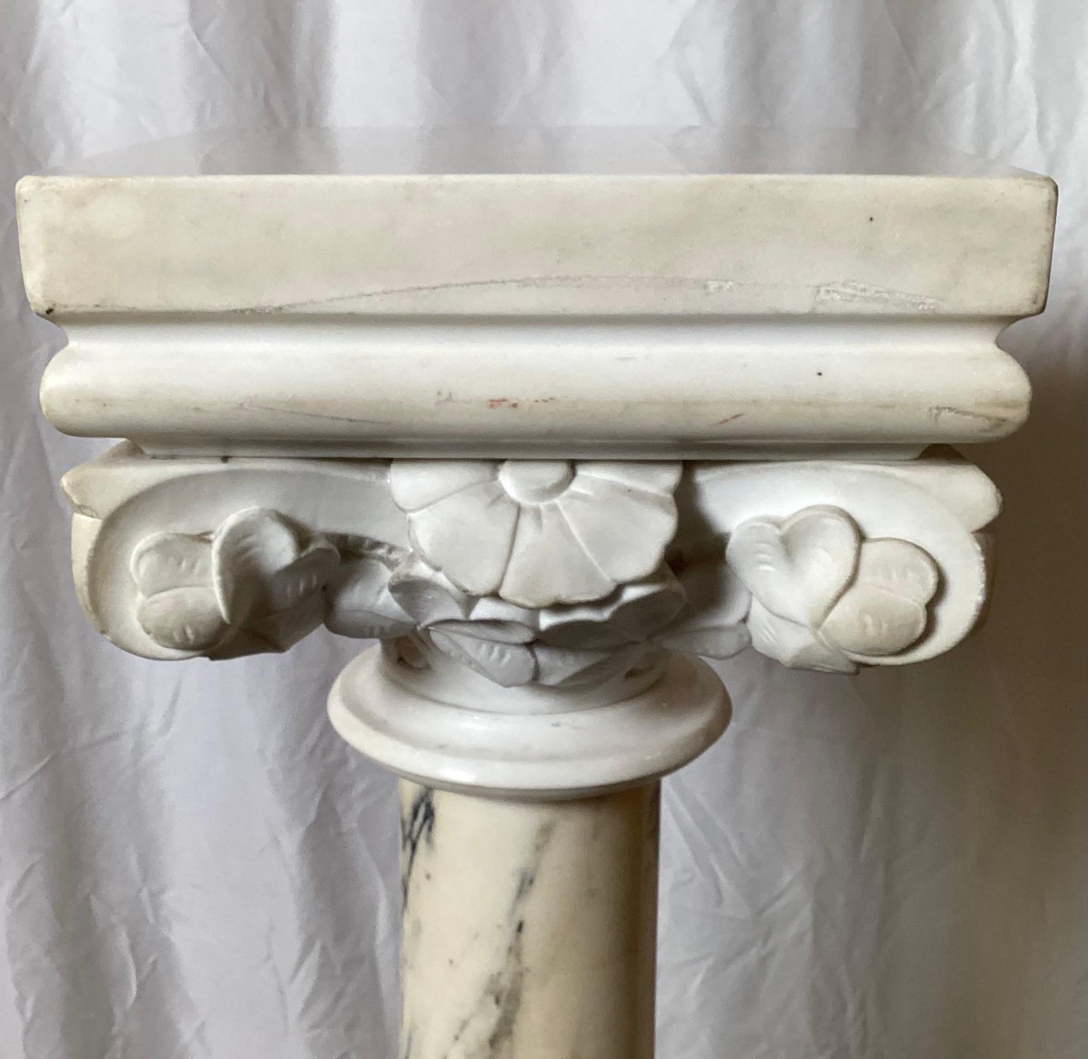Piédestal néoclassique en marbre de Carrare sculpté à la main, avec plateau et base en marbre blanc.  Le plateau feuillagé surmonte une colonne centrale veinée de gris et de noir, sur une base piédestale carrée. Le plateau se détache du piédestal en