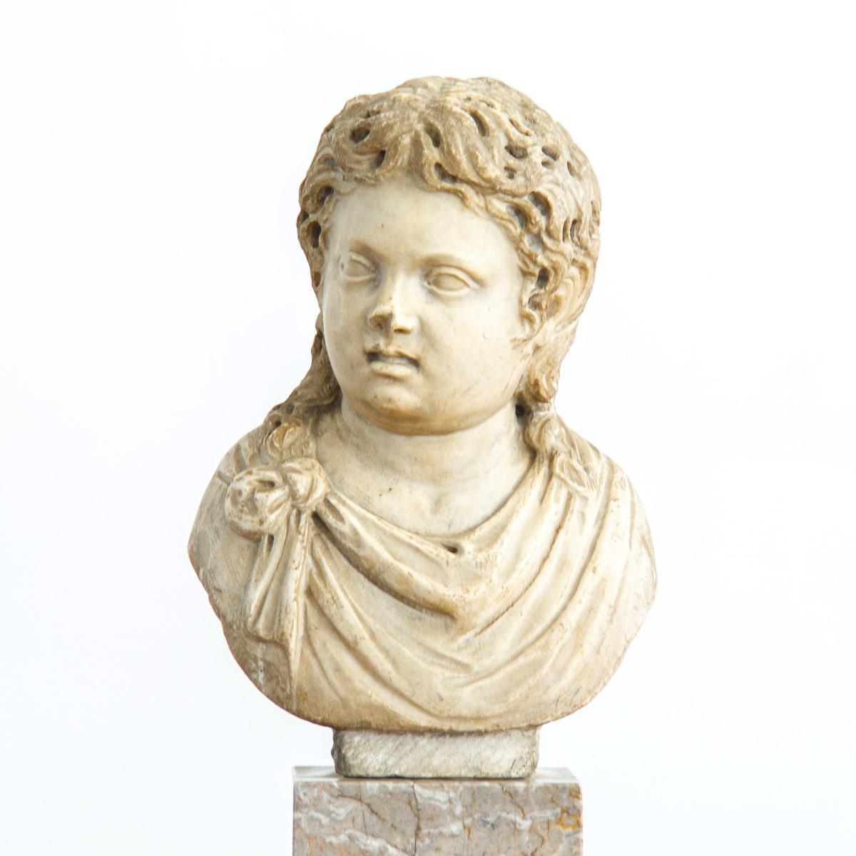 A 2nd century Roman bust of a young boy with curled long hair and classical dress. The nose is slightly preserved which adds to the busts character and is expected due to the age. The bust has its own socle which has been mounted on a younger marble
