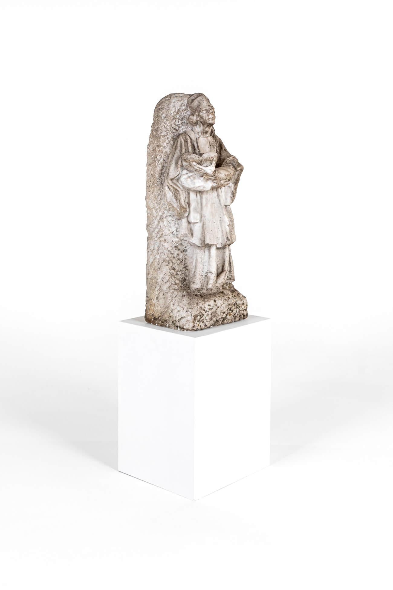 Un'imponente statua scolpita di un santo o di una figura ecclesiastica ricavata da un unico pezzo di marmo bianco.

La figura maschile in paramenti clericali guarda in alto e tiene un libro aperto tra le braccia e le mani incrociate ma rilassate del