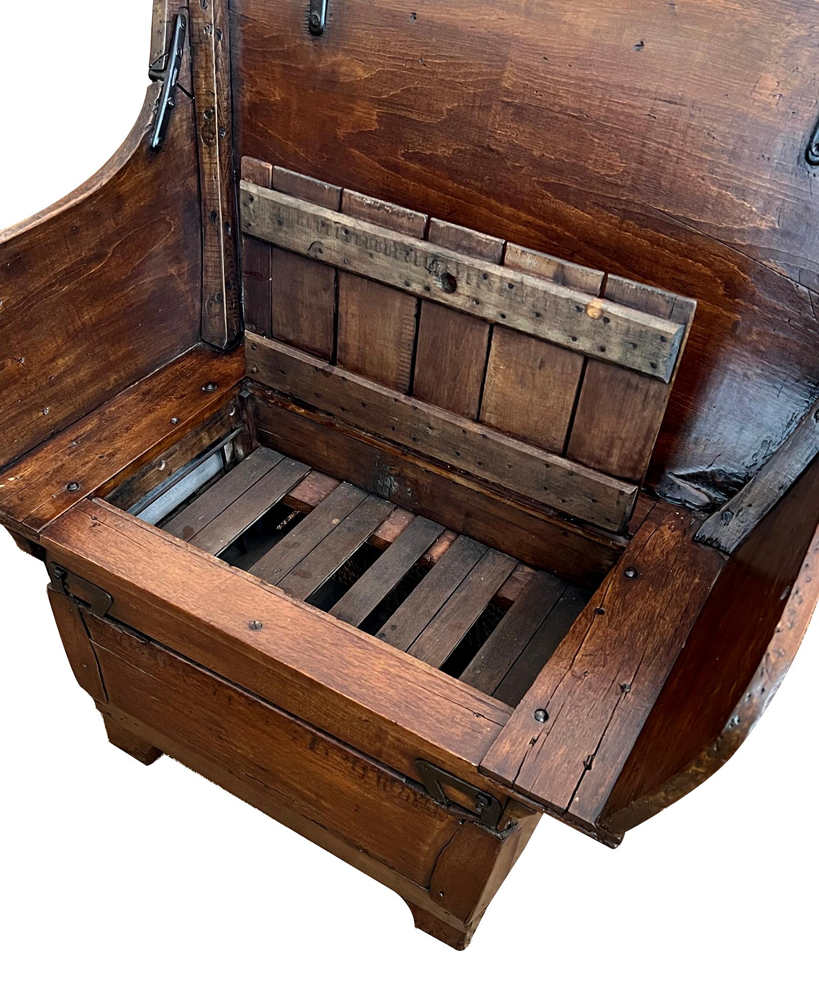 of generous proportion with flared back and arched crest above a seat with a small hinged compartment; the seat back with carved paneled reserves; raised on a wooden base with later supports; the whole fitted with iron hardware; new channeled
