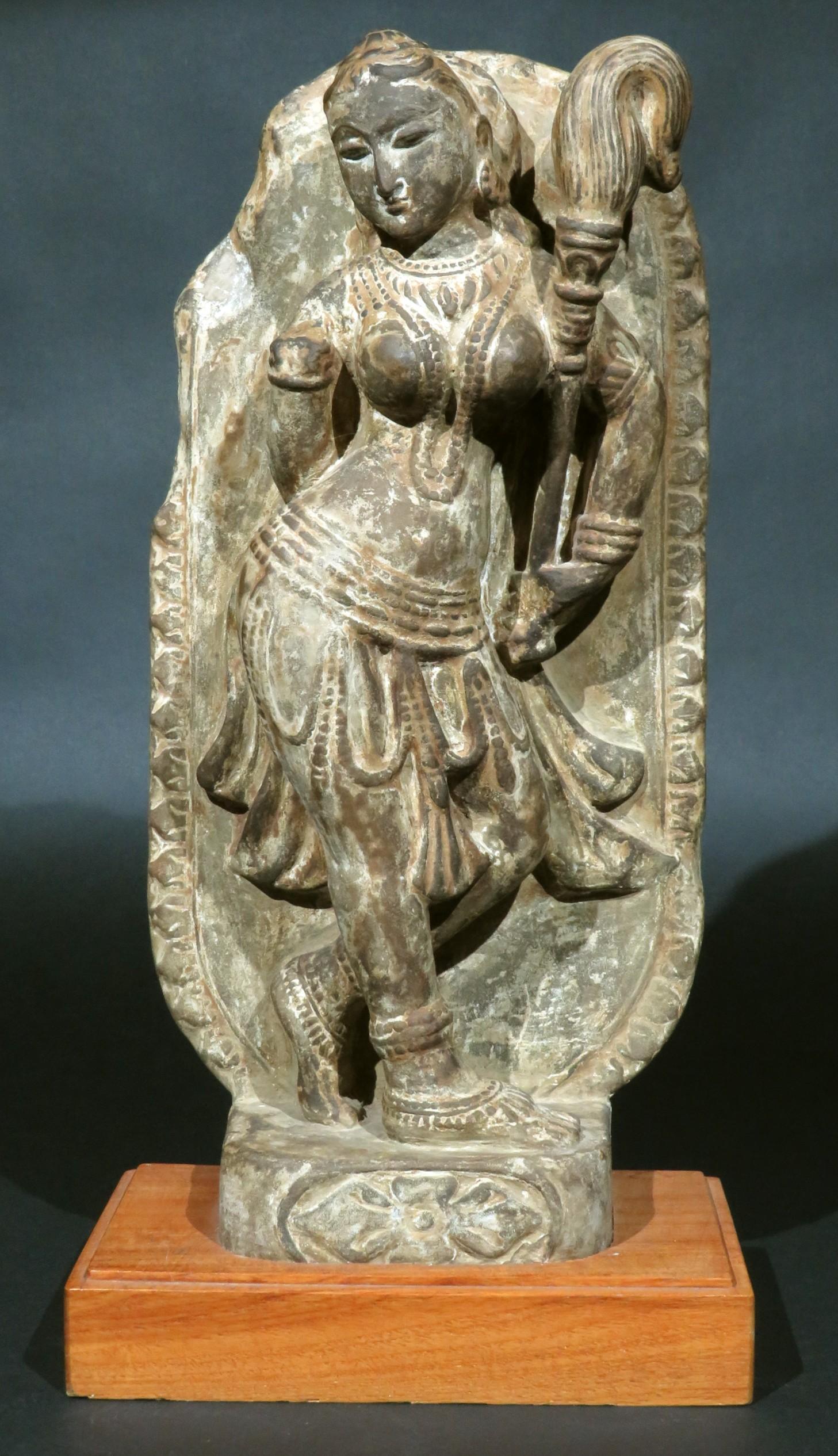 The Hindu Goddess Parvati - wife consort of Shiva and Goddess of beauty, fertility & marriage, shown carved in high relief issuing from a gray schist stele with a petal carved border. 
The semi-clad figure richly adorned with a beaded necklace,