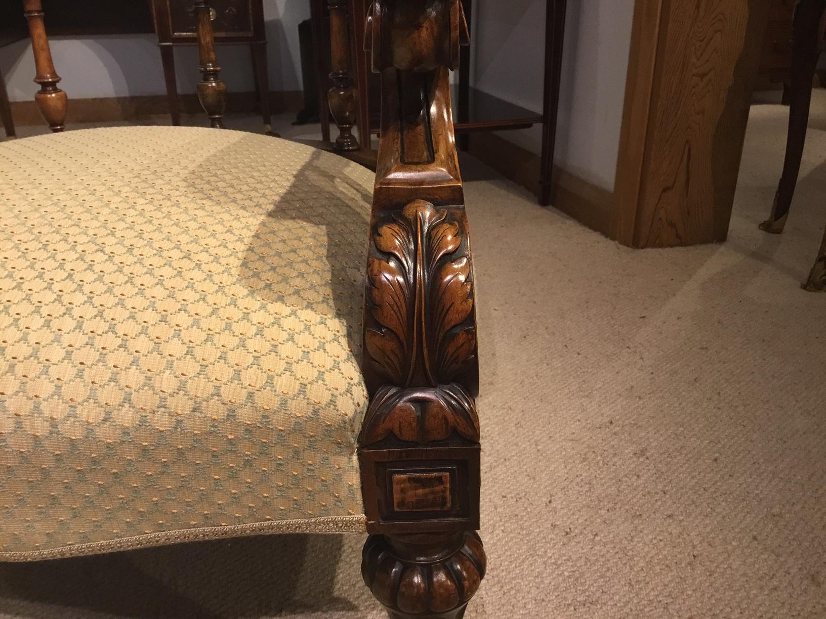 A carved walnut Victorian Period love seat/conversation seat. Each side constructed using solid walnut with curved padded back supports, acanthus carved scrolling arms and finely turned walnut spindles. Having sprung seats newly upholstered in a