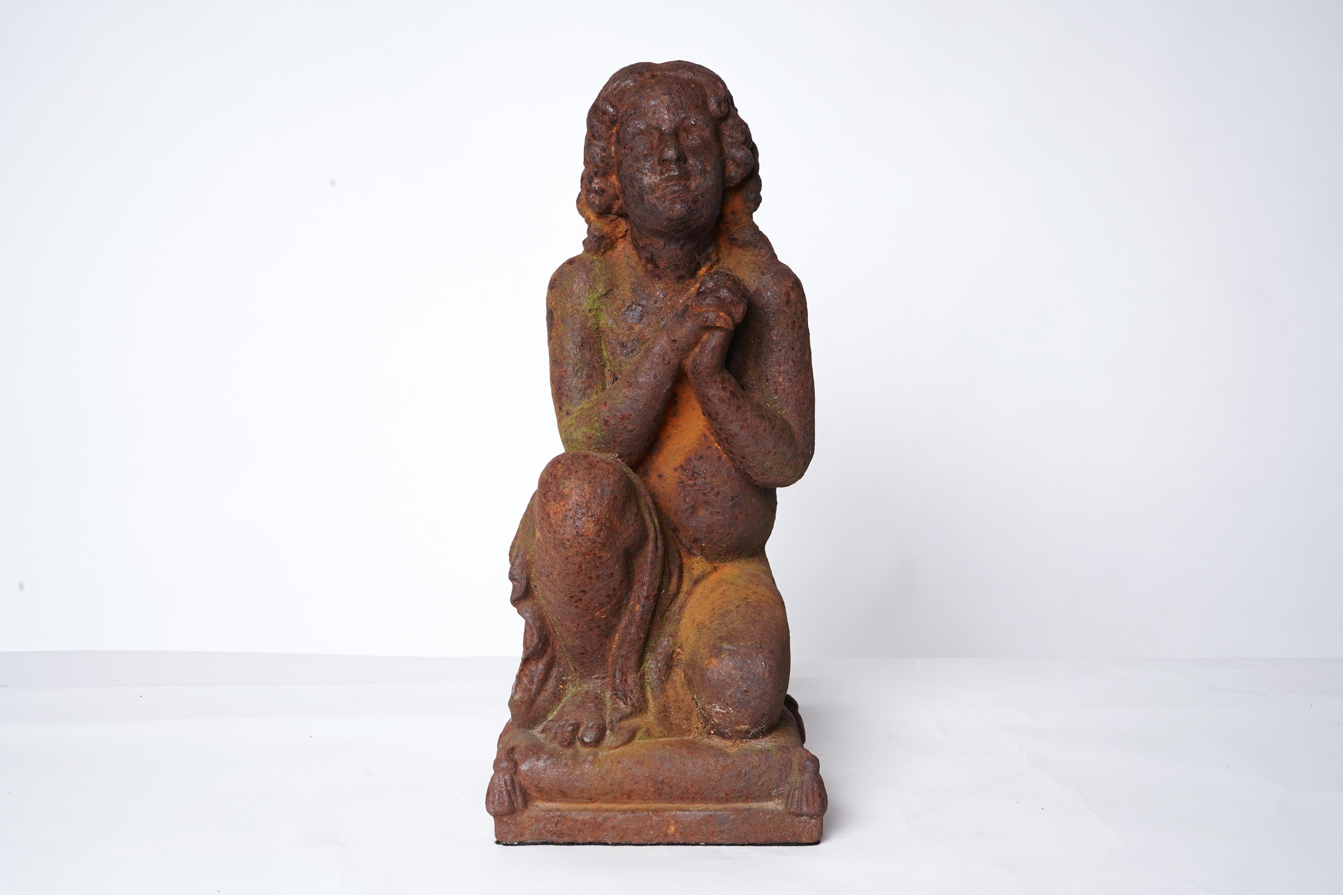 This cast iron sculpture depicts a young child in a praying pose. It was made as an outdoor garden decoration and retains some original paint. Its highly rusted state suggests long-term outdoor exposure.