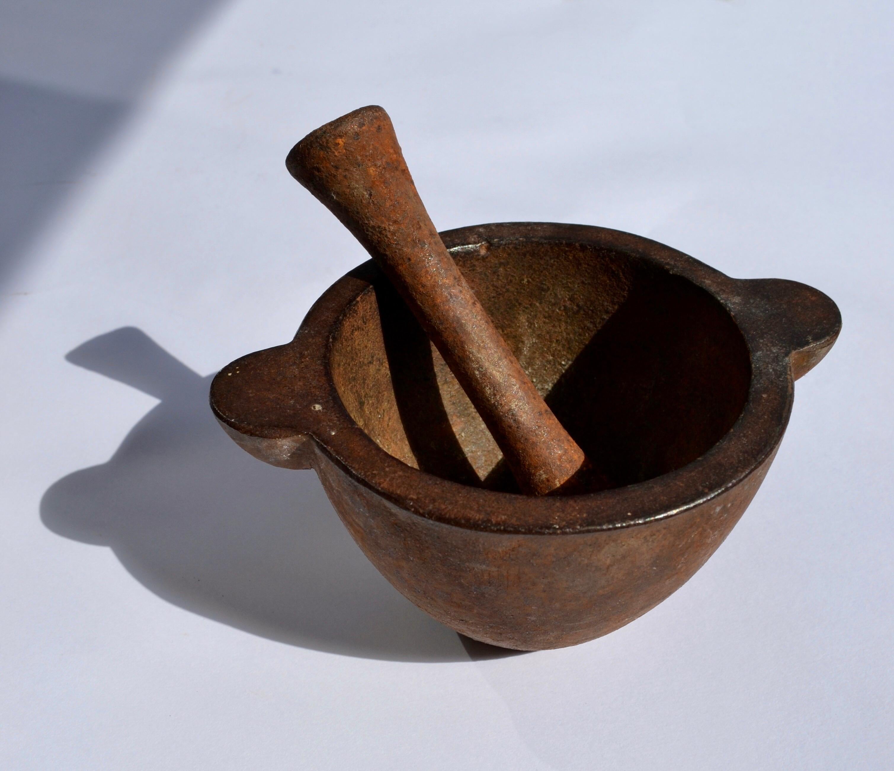 Un mortaio in ghisa con il suo pestello originale, utilizzato nelle farmacie all'inizio del XX secolo. Questo utensile, progettato per macinare sostanze medicinali, presenta una bella patina, a testimonianza del suo uso e del periodo in cui è stato