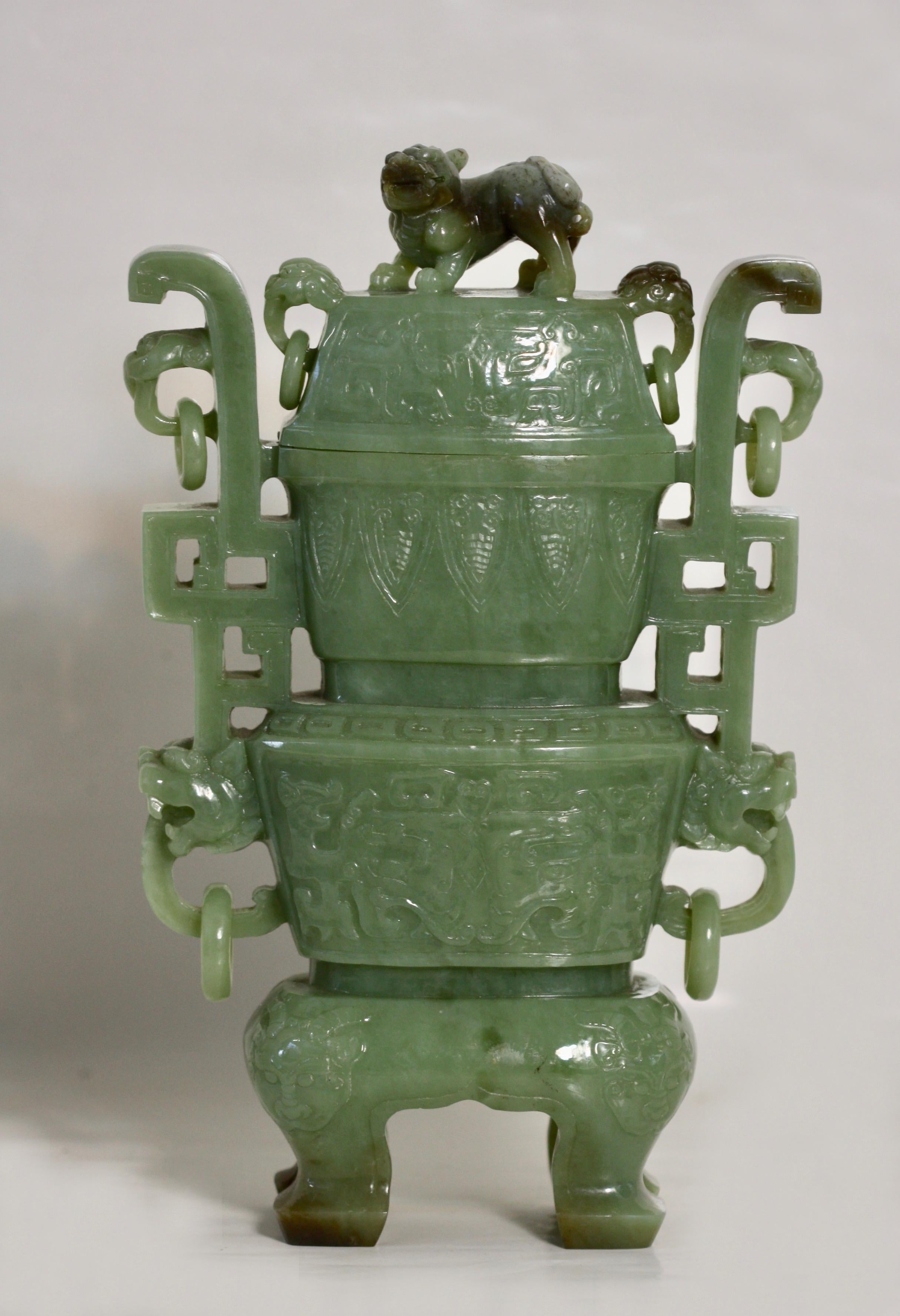 A celadon jade vase and cover, Chinese
the flattened baluster body rising from a splayed foot to a waisted neck, flanked by a pair of foliate loop handles suspending loose rings, each face worked in low relief with a medallion enclosing floral