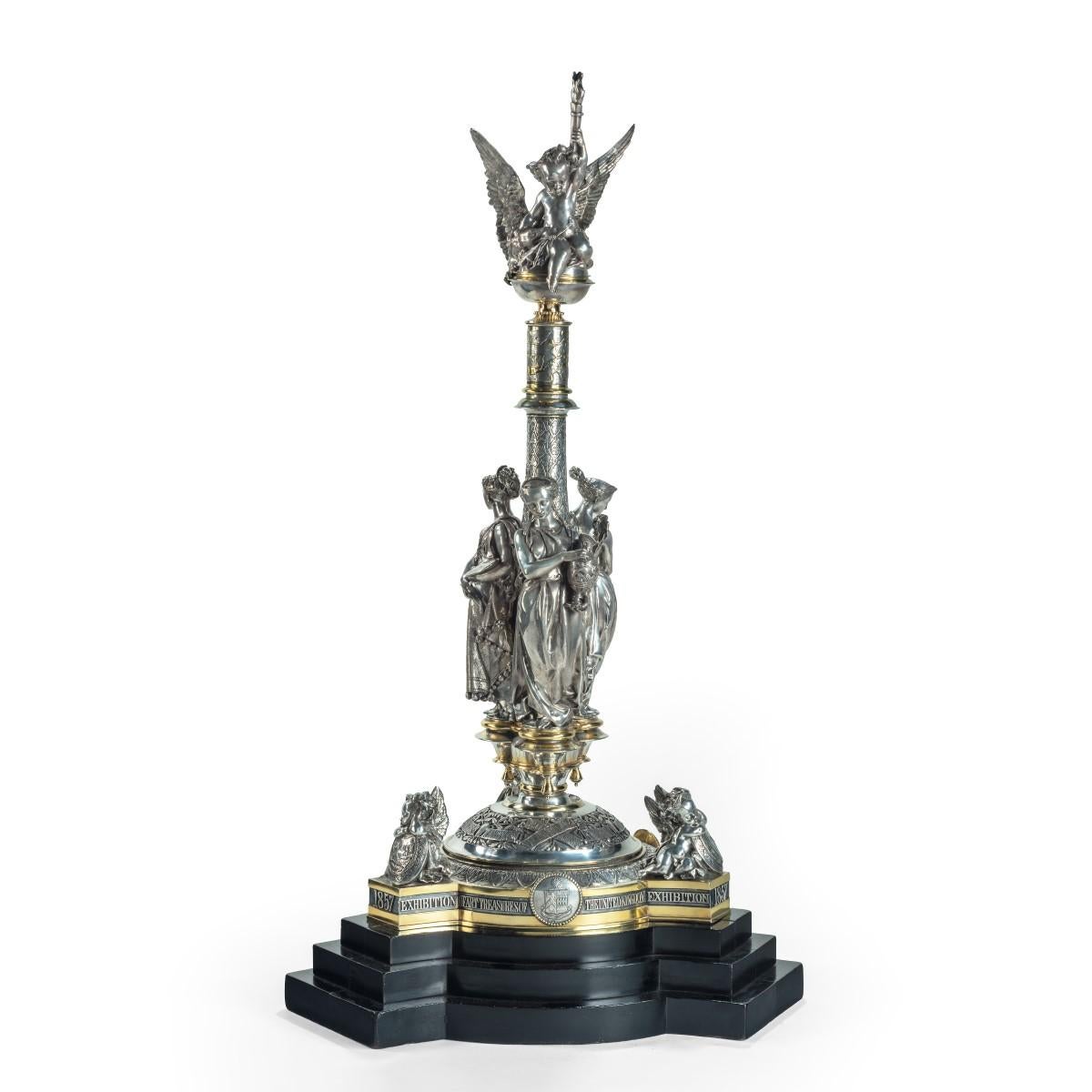J. B. Waring describes this oxidised silver Testimonial as follows: “The Manchester Art-Treasures Testimonial is surmounted by a figure of genius contending with an eagle, around which are allegorical figures of Painting, Sculpture and Industrial