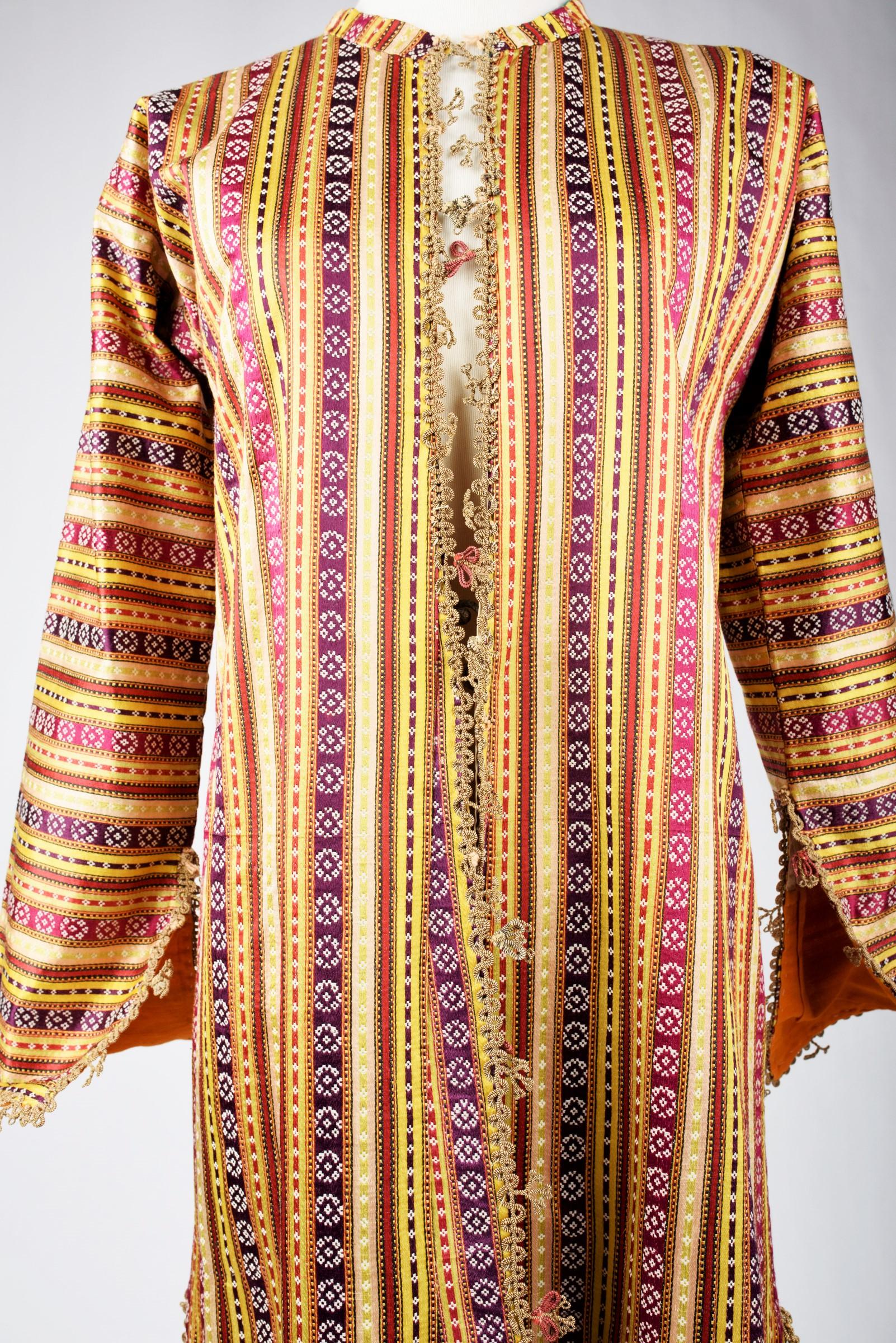 Circa 1900-1930
Ottoman Empire

Long ceremonial coat, kaftan or Entari in silk and cotton satin with fine stripes drawn with rosettes. Crew neck cut, long sleeves with slits at the wrists and two side slits, fully lined with crests of golden blade