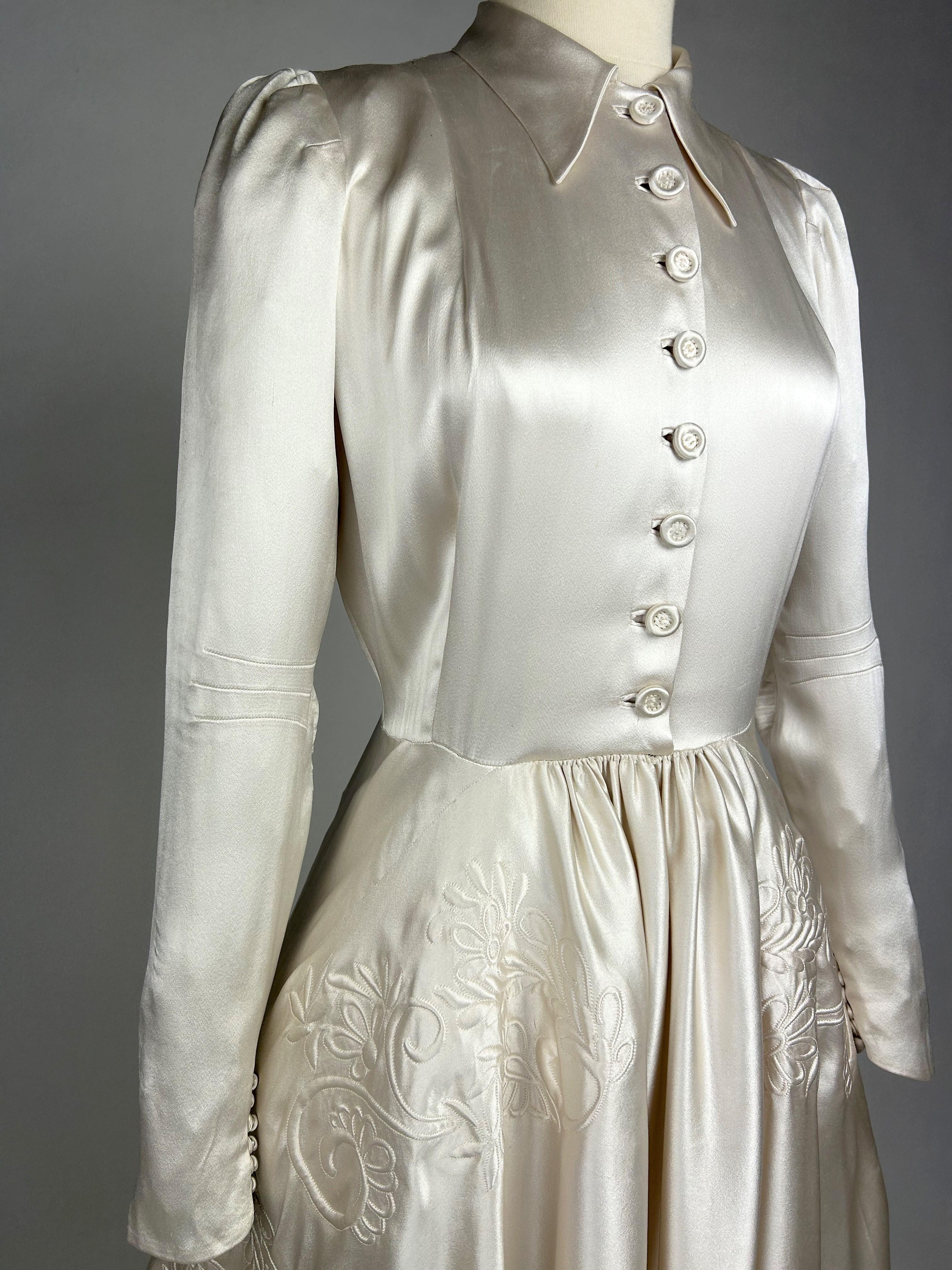 Circa 1938-1942

France

Wedding dress with long train in champagne-coloured Duchesse satin. Fluid cut with a strapless blouse with a folded collar, long sleeves with darts and double buttoning in front and back. The back is extended by a single