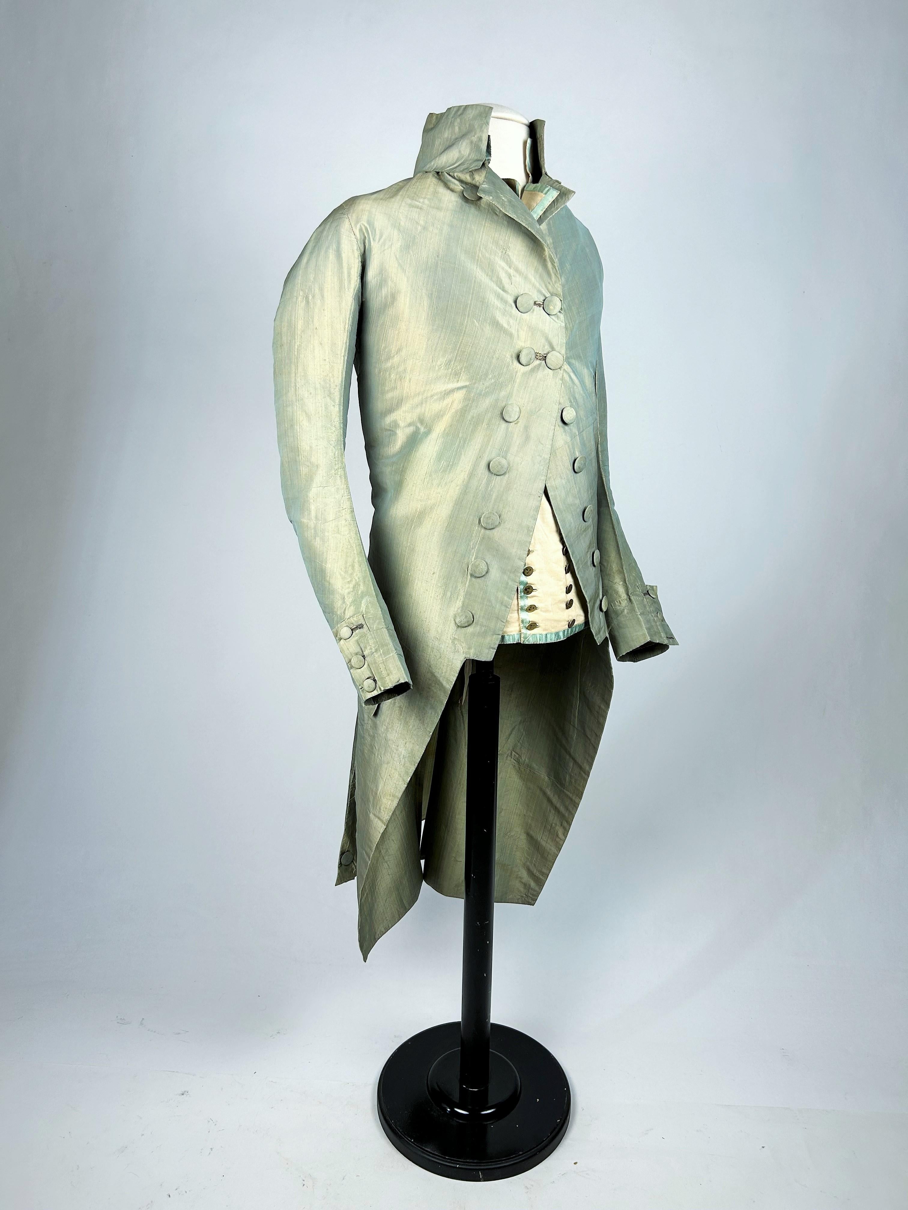 Circa 1785-1790
England

Summer suit in changeable taffeta and its cotton waistcoat, set collected in England. Frockcoat, high collar, long angled sleeves in blue and yellow changeable taffeta giving a subtle greenish greyness. Fitted cut with