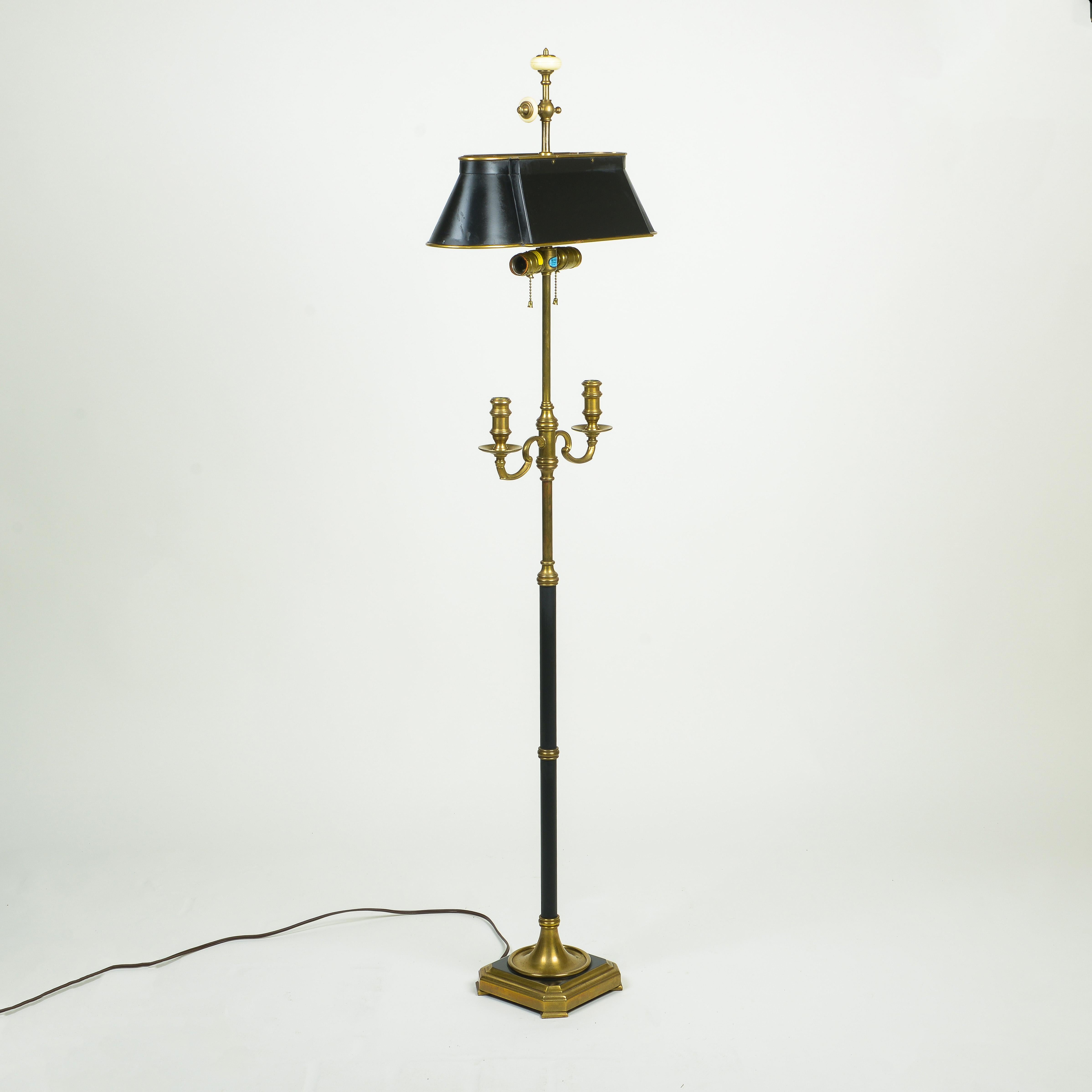 The oval bouillotte shade set above two bulb sockets; the columnar brass and black enamel stand issuing two outward scrolling candlearms; on a square stepped base.