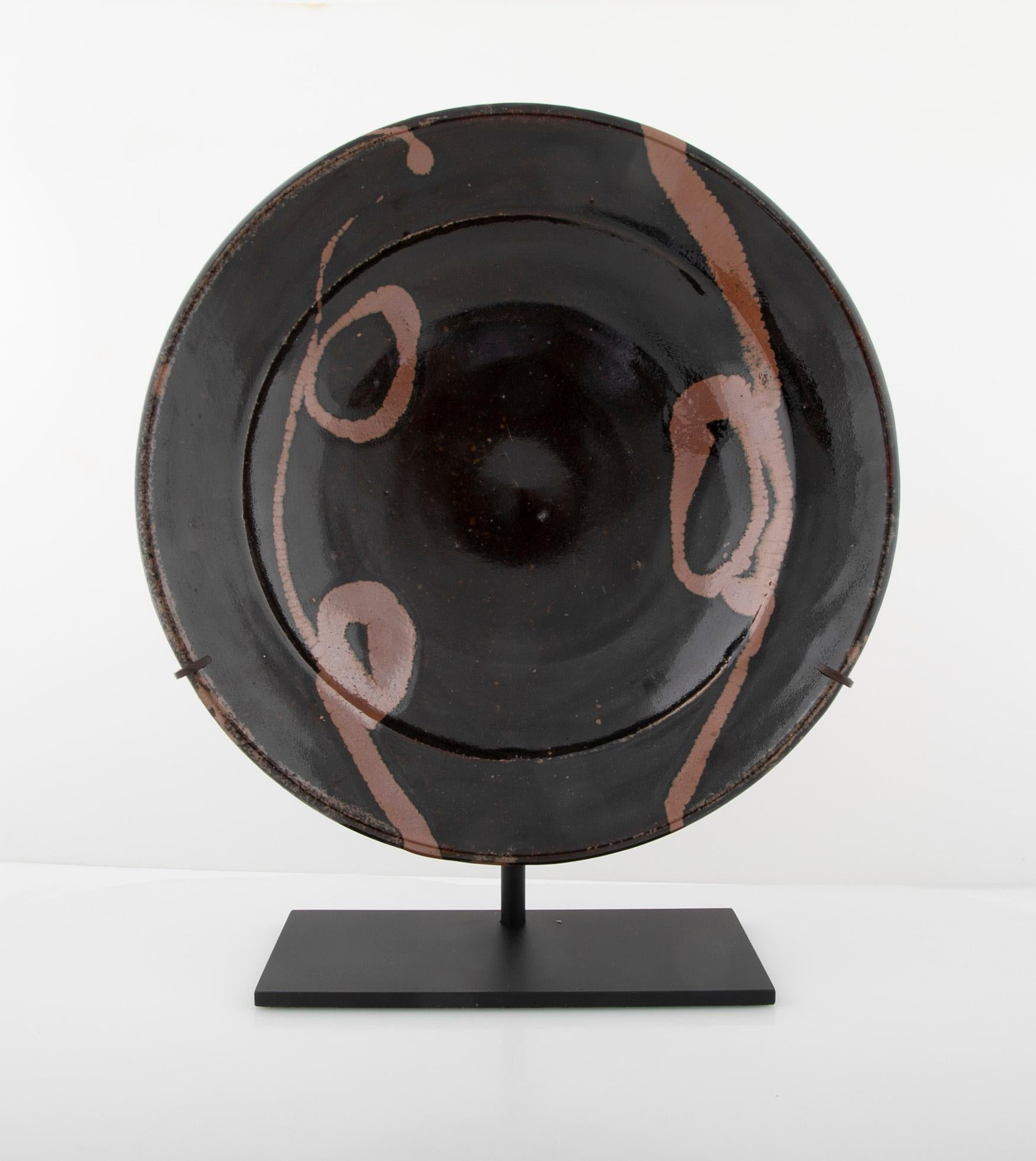 Shoji Hamada Japanese clay charger with black glaze and terracotta toned glazed decoration, circa 1960s. On contemporary stand. The piece is unsigned and as such cannot definitively said to be by Shoji Hamada. This is not uncommon for his