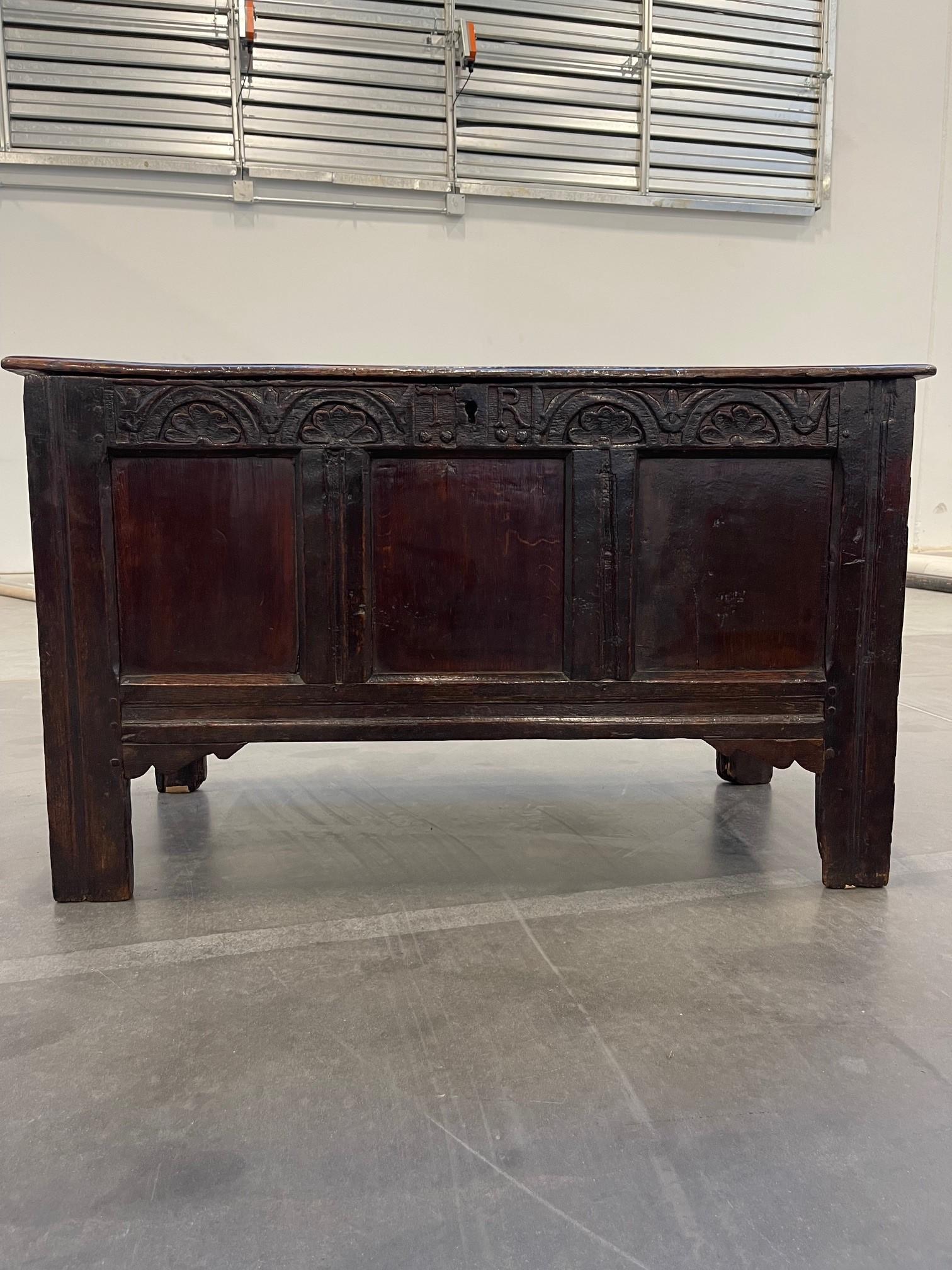 A wonderful Charles II Carved Oak Coffer Circa 1670, with three front plain panels sitting below a carved foliage freeze. Initialed TR on each side of center lock with a two plank hinged lid, (hinges appear to be original) sitting on stile feet. The