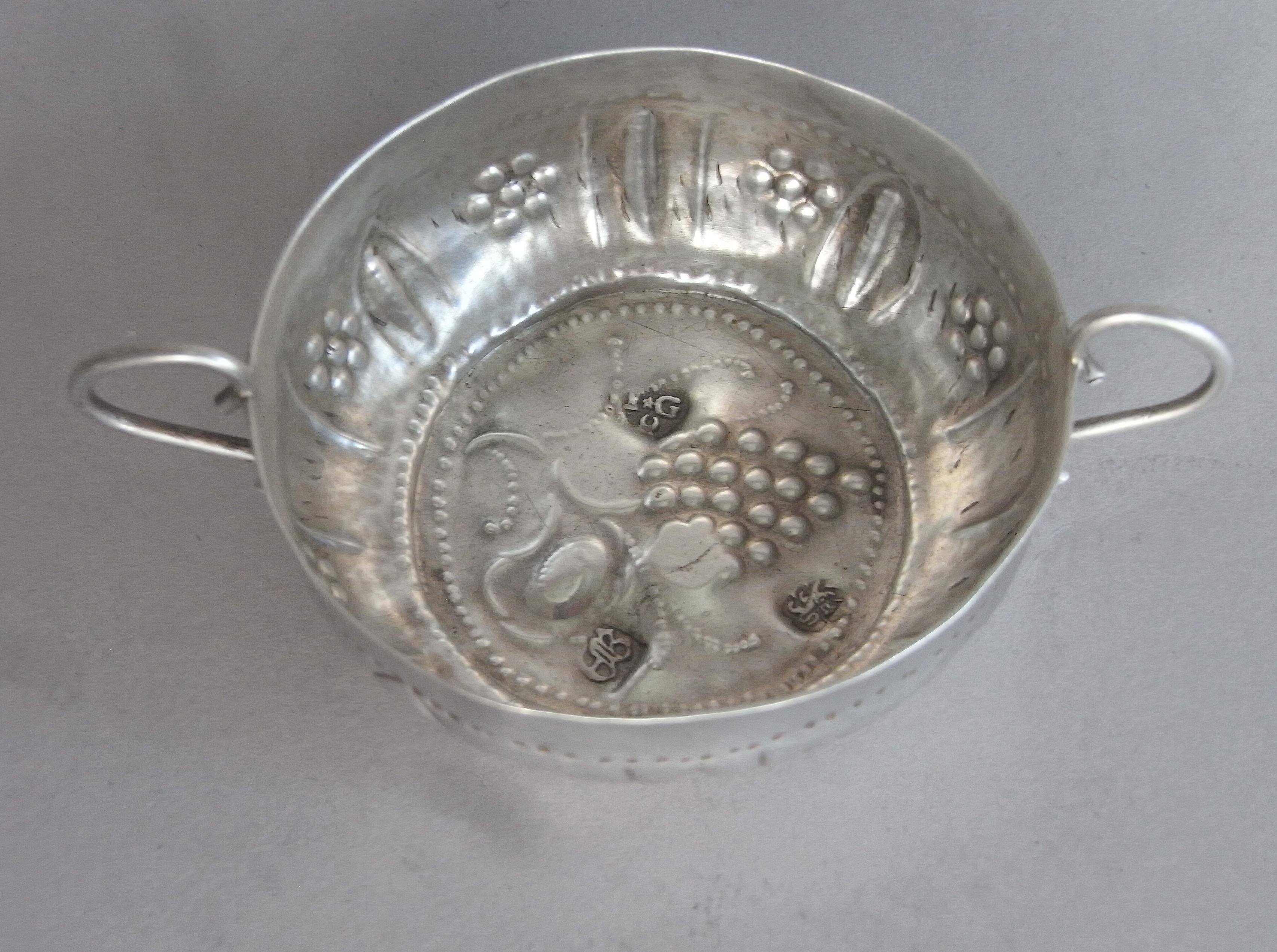 The wine taster stands on a narrow circular foot and has slightly baluster sides, and everted rim. The sides are decorated with punch bead bands, as well as stylized flower heads and foliate spears. This example has wirework 