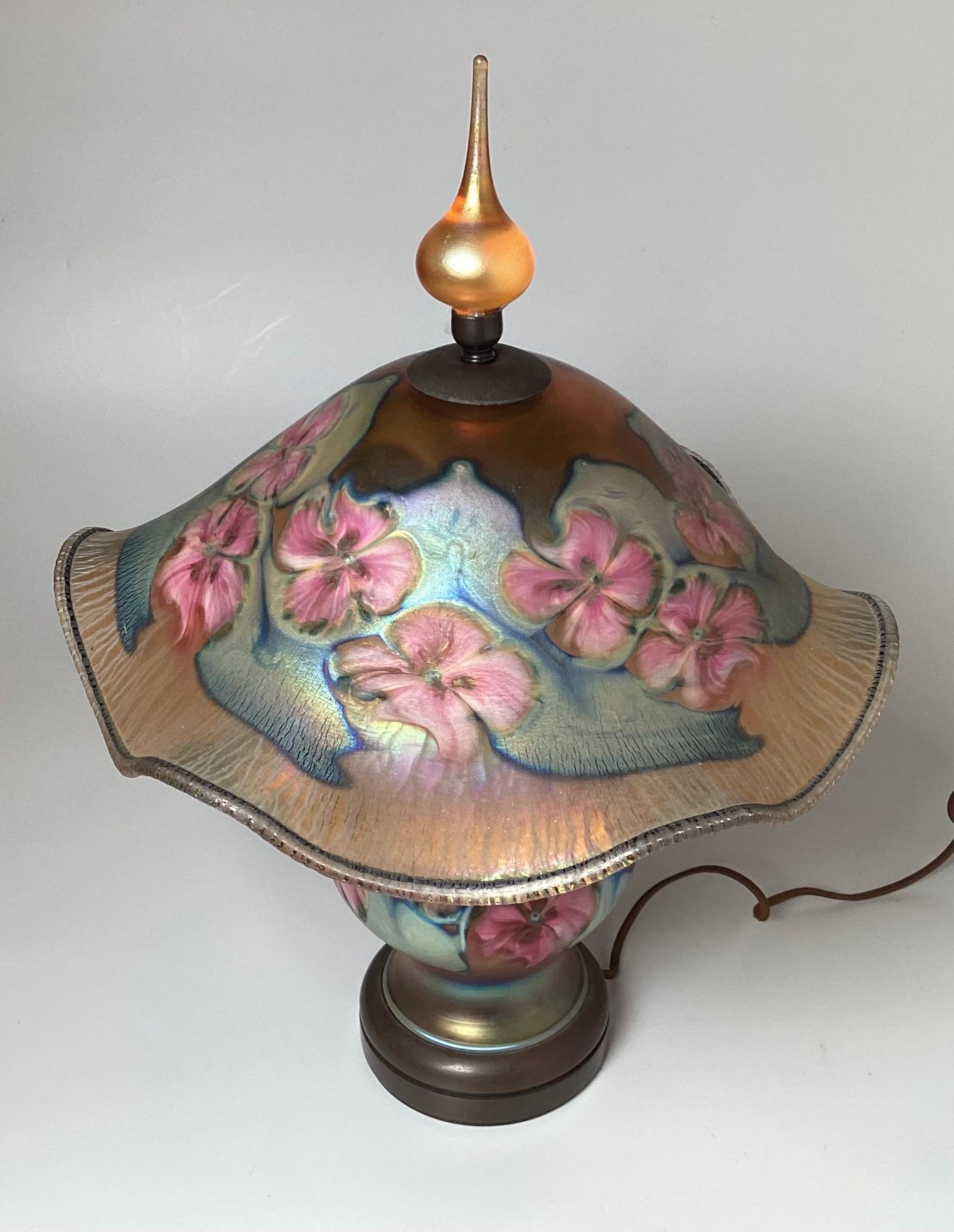 A beautiful hand made art glass lamp with gold iridescent ground and border with blue base, multi floral design and original finial. Signed Charles Lotton 1993 at top of shade 

Charles Lotton was born in a little town in Southern Illinois, after