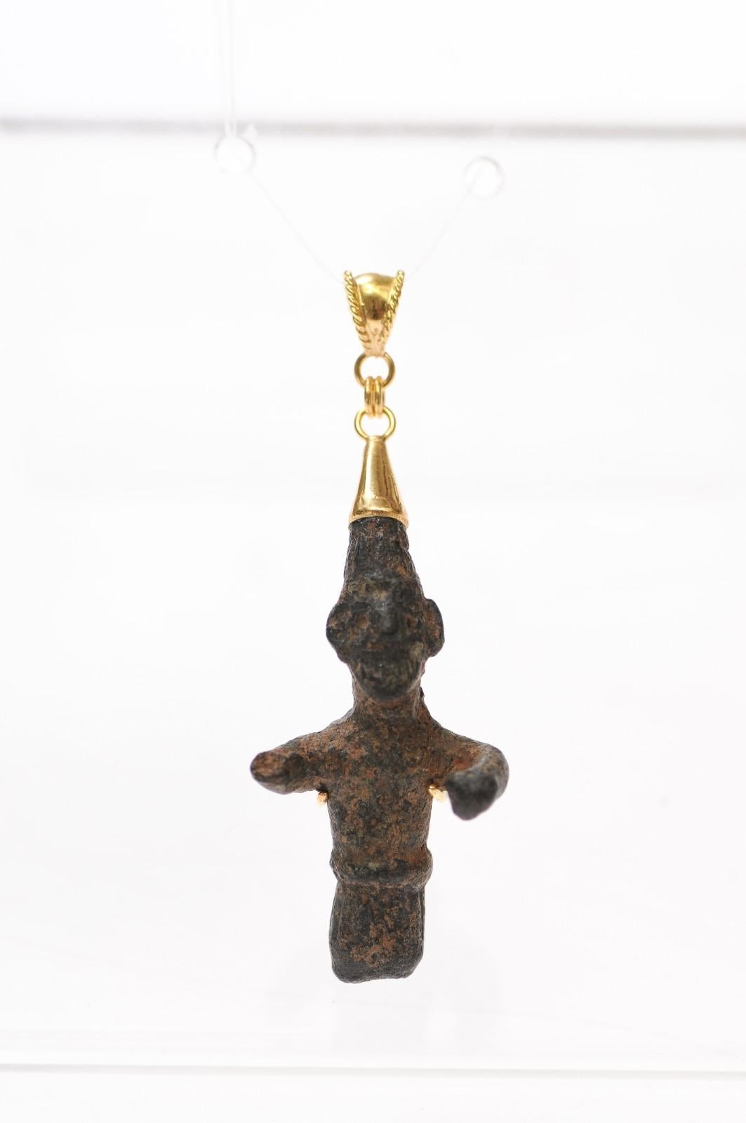 A charming bronze figure from the Ancient Roman Empire fashioned into a pendant trimmed with 18 karat gold accents and bail. There is a marvelous patina that demonstrates the charm's age. This is dated approximately from the 1st to 3rd Century AD
