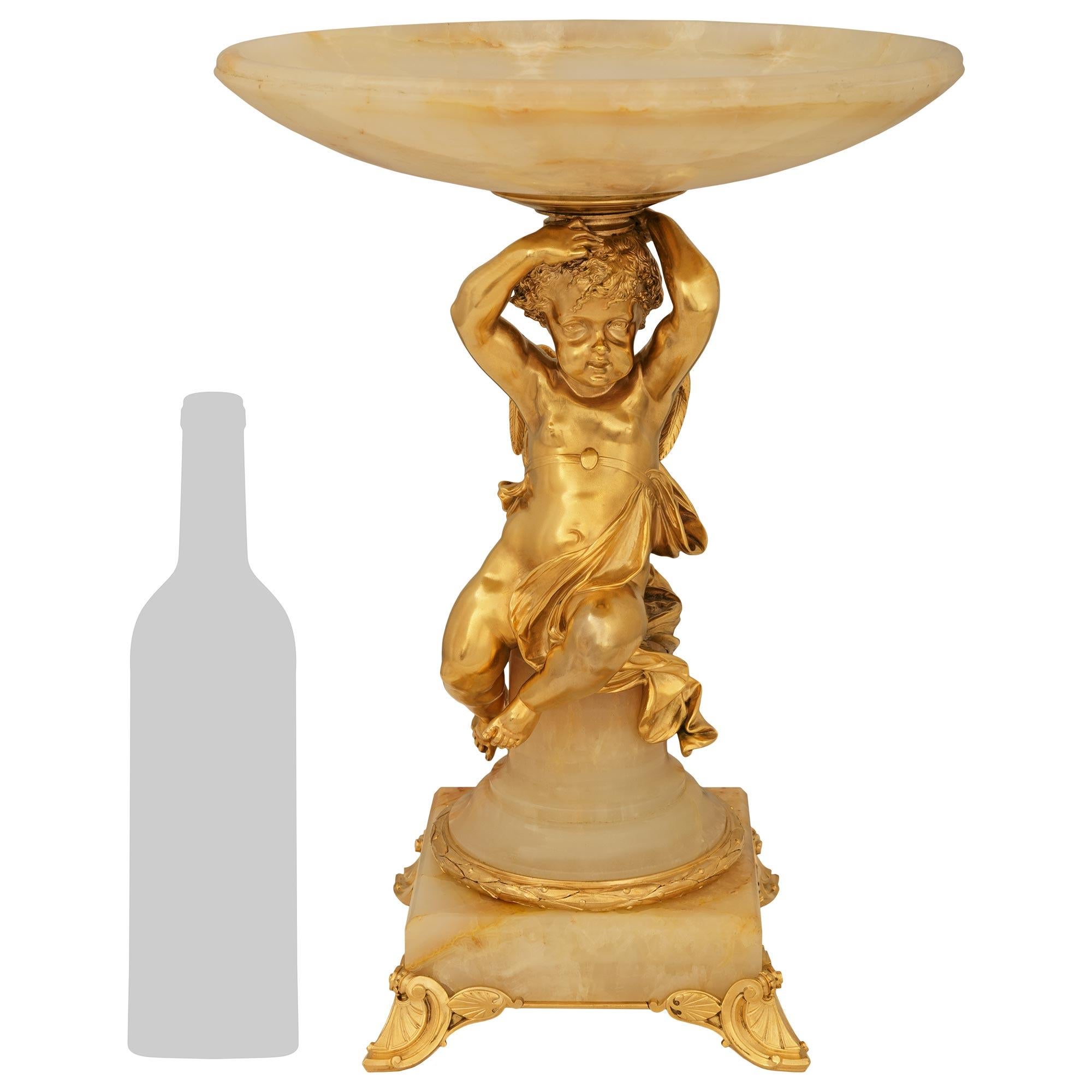 Charmant centre de table en bronze doré et onyx de haute qualité, de style Louis XVI, datant du XIXe siècle. Cette pièce maîtresse des plus élégantes repose sur quatre pieds à volutes en bronze doré qui soutiennent une base carrée ornée d'un bandeau