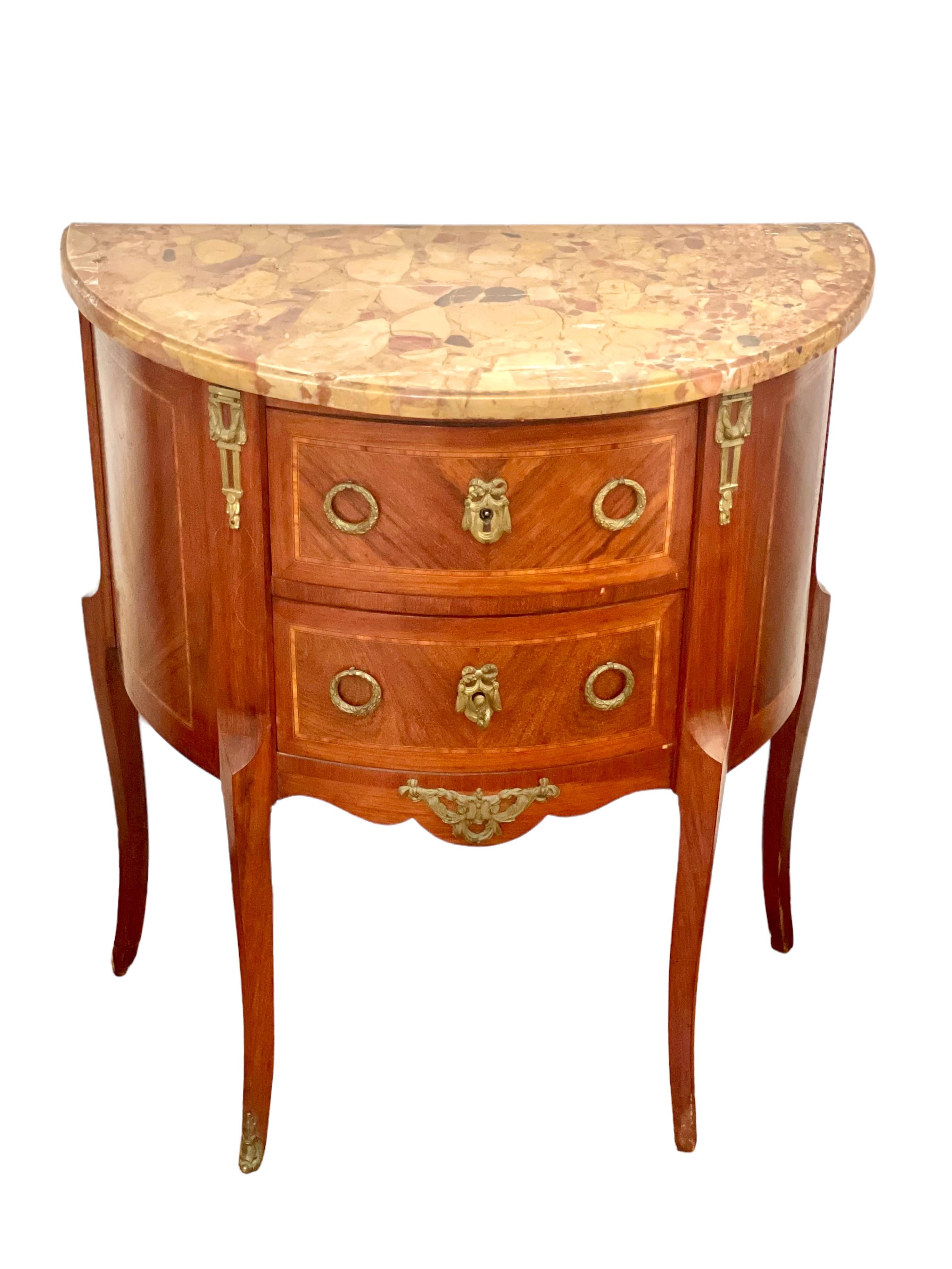 A charming, French Louis XVI transitional style demi-lune two-drawer commode, with an intricate inlay of cross-banded patterns across the facade and sides. Fitted with fine, gilt bronze mounts, drawer pulls and feet, and topped with marble, this