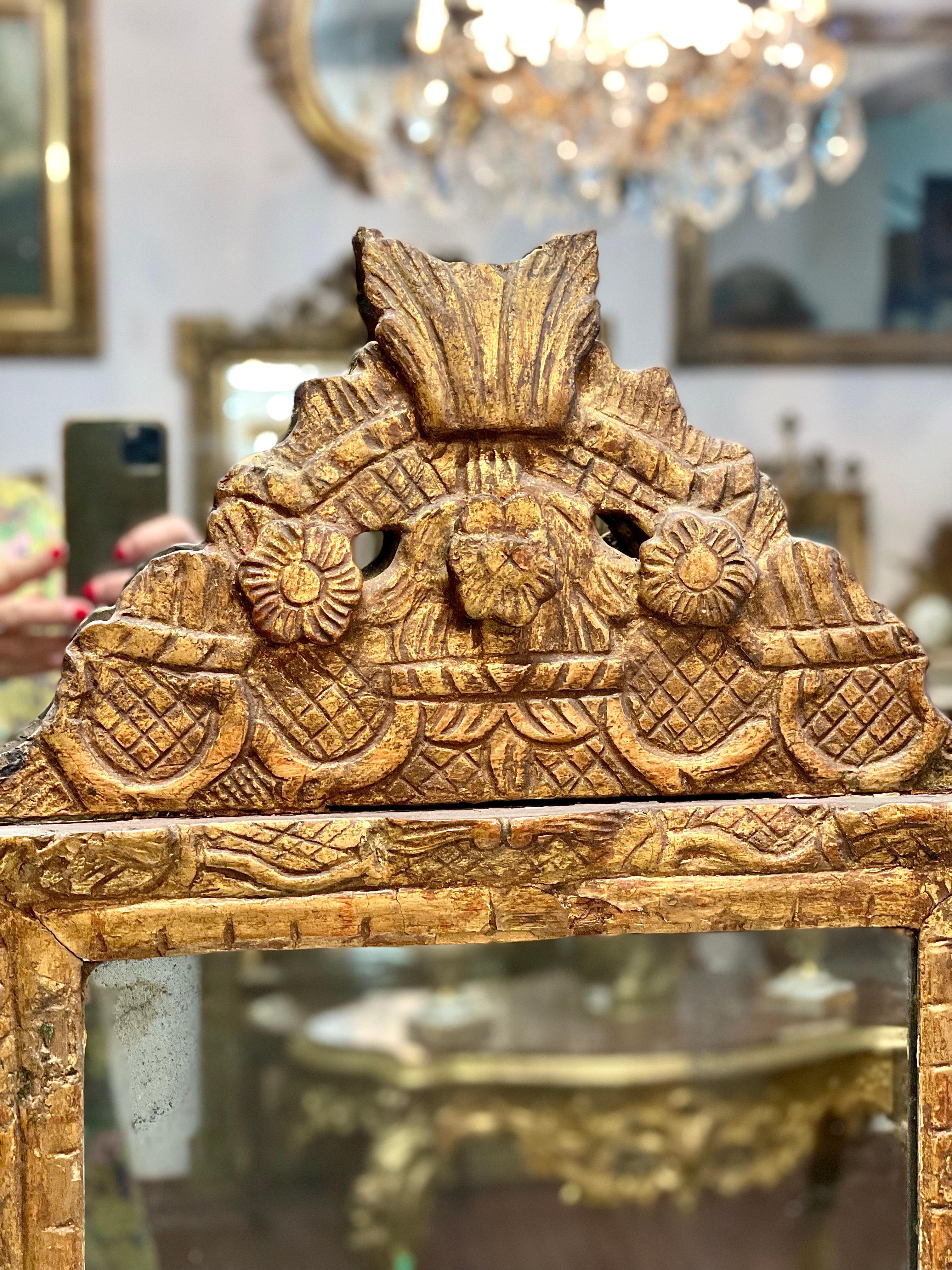 A charming little 18th century, French Régence period boudoirstyle  mirror, in gilded and carved wood, with an ornate pediment featuring a trio of flowers protruding from a latticework background. The carved decoration is continued around the frame