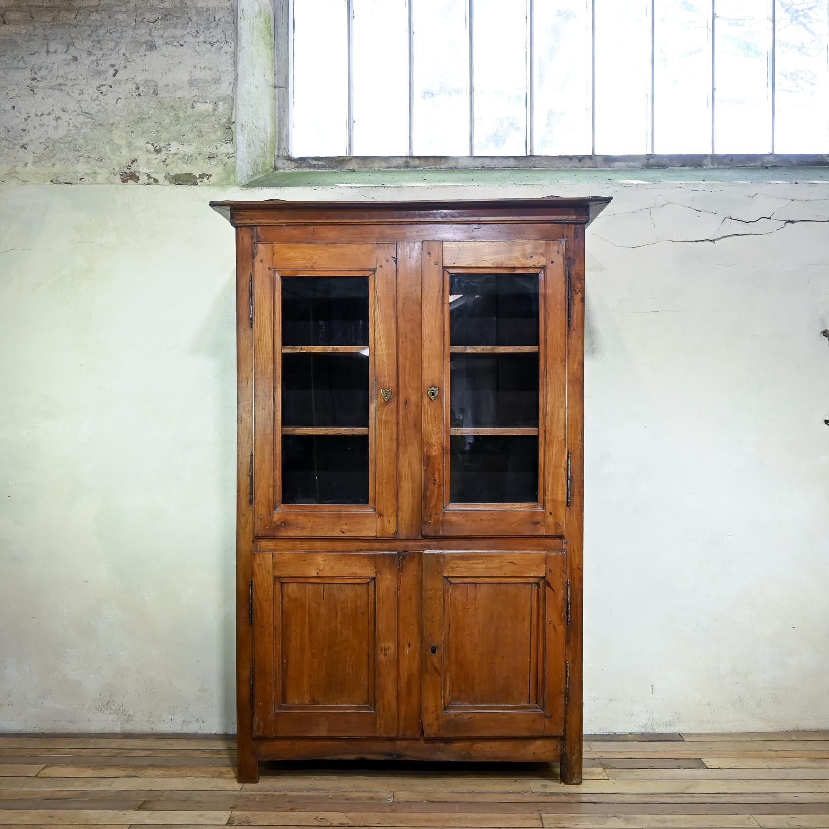 A charming Mid-19th Century French cherry wood cupboard. Displaying a simplistic moulded cornice above a pair of inset glass doors with a further pair of panelled doors below featuring three fixed interior shelves. Raised on block feet.
