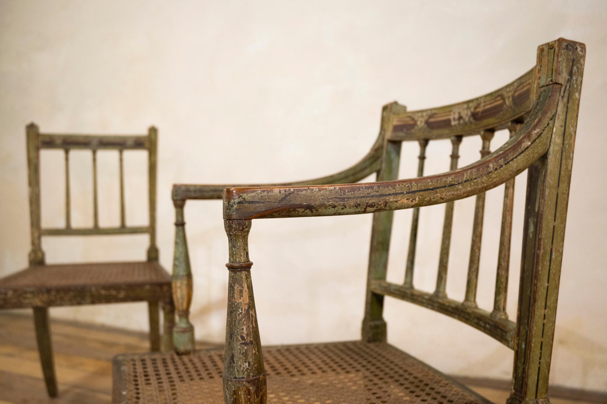 A charming near pair of Regency green painted occasional chairs. Retaining original delicate painted decoration framed with elegant black painted banding. Presenting turned back spindles - with charming detailing throughout. The elbow chair displays