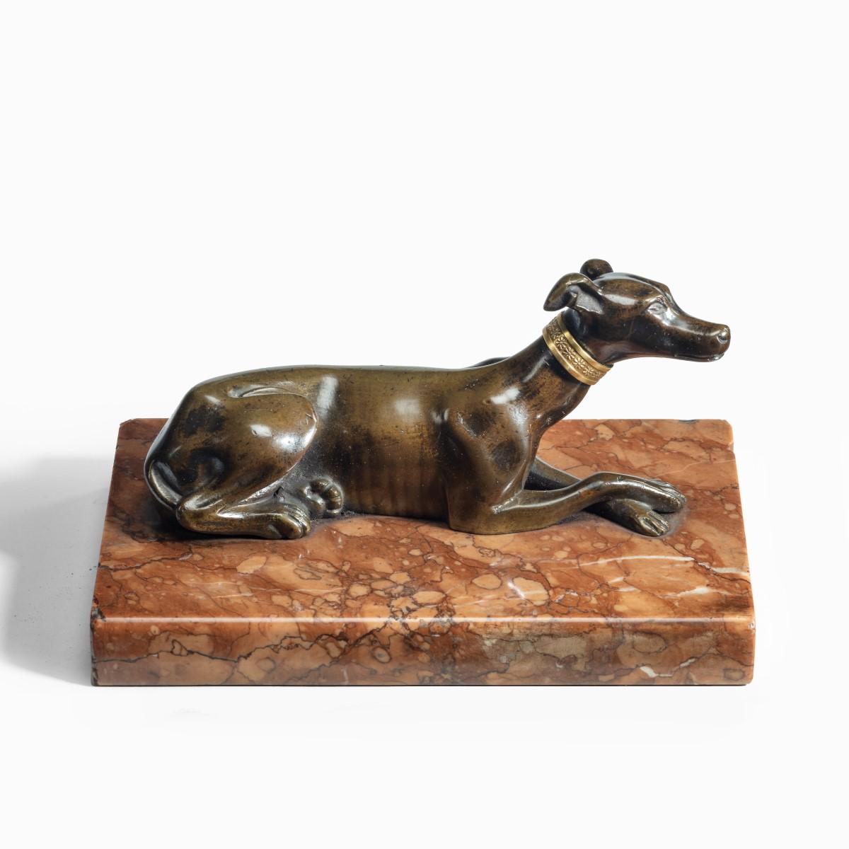 A charming Regency greyhound paperweight, the recumbent dog with its front paws crossed and wearing gilt collar picked out with flowerheads, all on a marble base. English, circa 1815.
