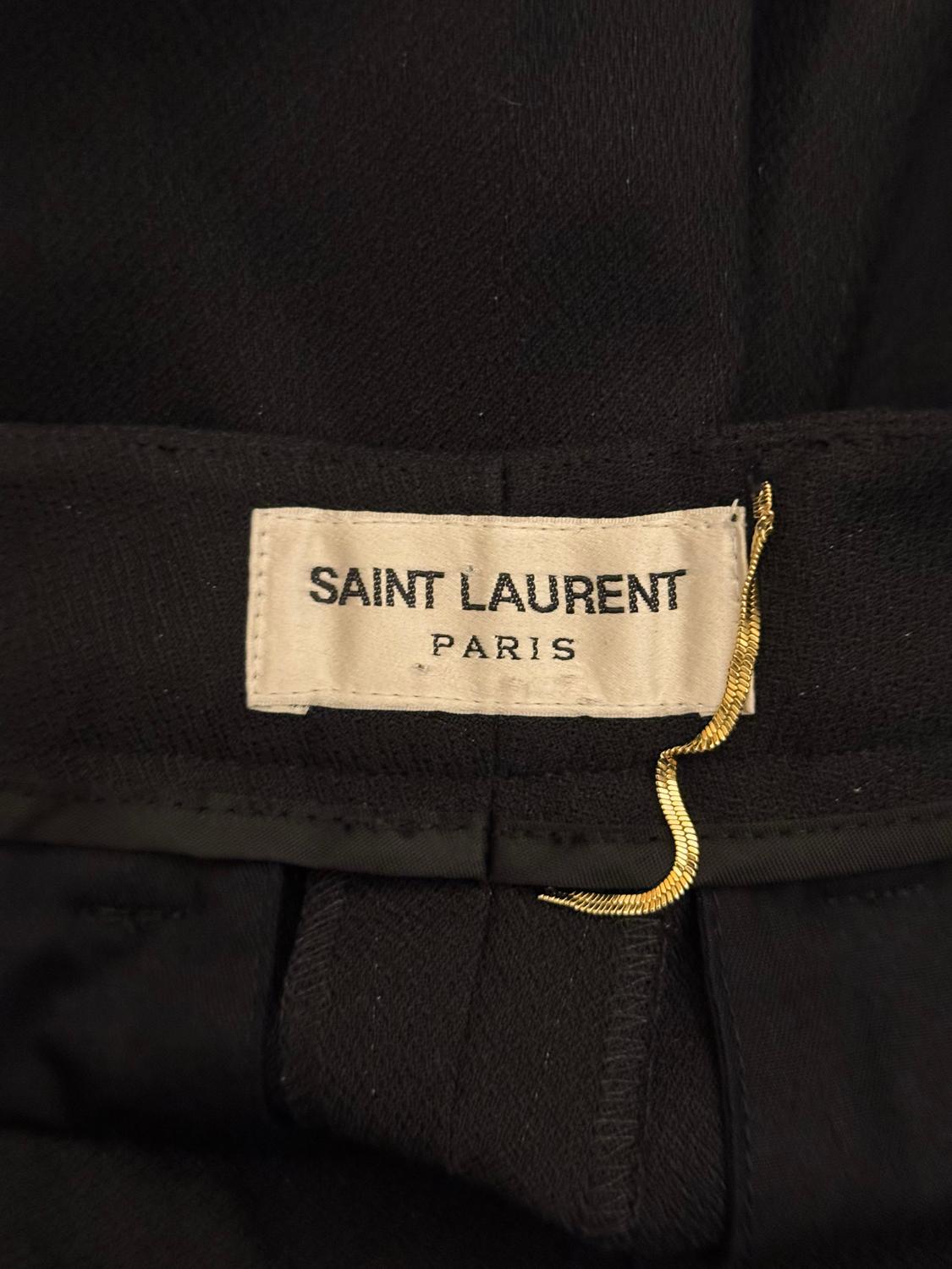 Unos pantalones negros chic de Saint Laurent Paris. Los pantalones tienen cremallera delantera y aros para el cinturón. Tienen un bolsillo a cada lado y bolsillos de imitación en la parte trasera.
Medidas: Cintura 25'', interior de la pierna 36''