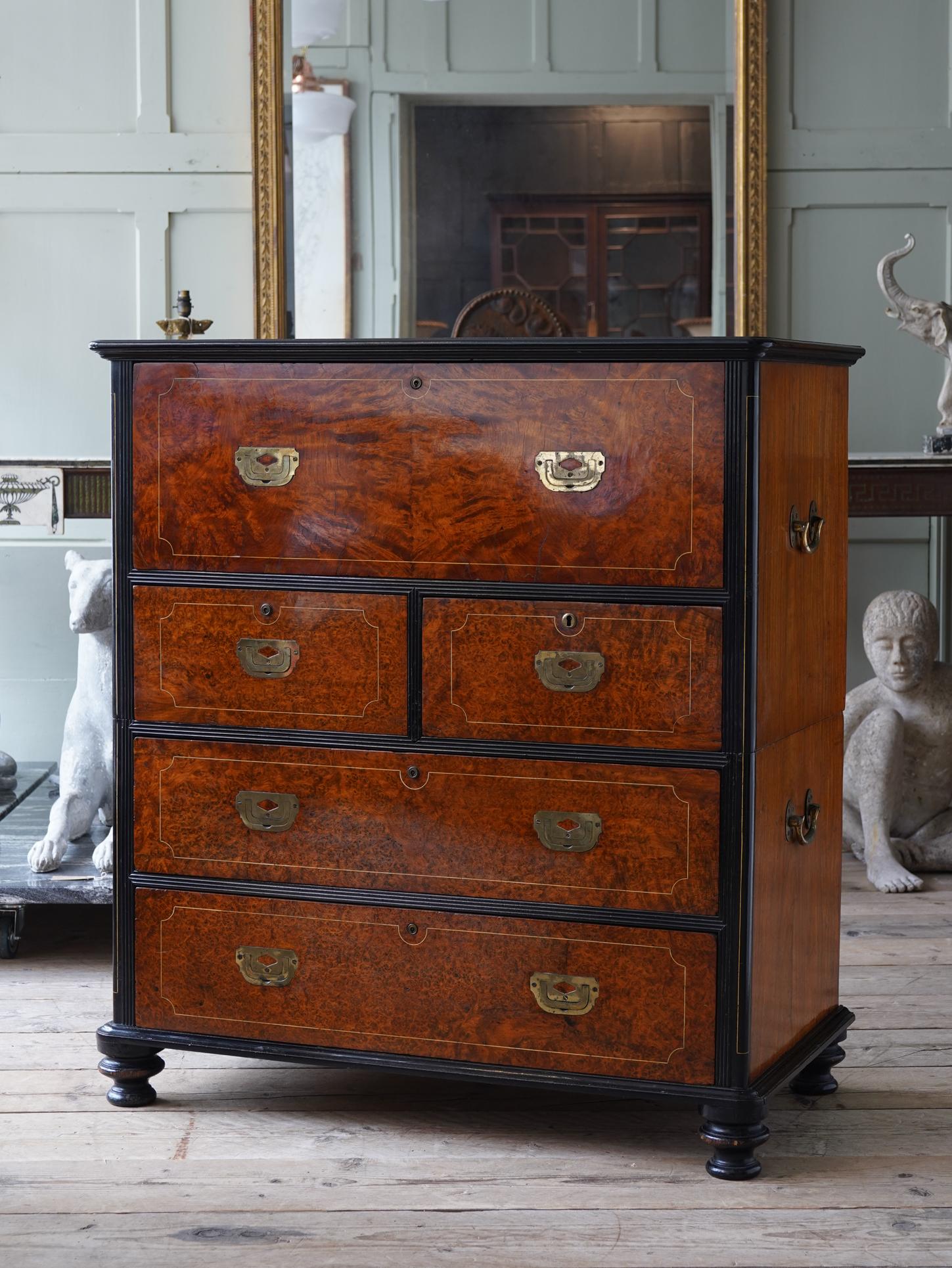 A mid-19th century China trade amboyna veneered camphor wood secretaire campaign chest.

The chest has an ebony reeded frame and bun feet, constructed in two parts with brass carrying handles to both sections. The drawer fronts have flush gilt