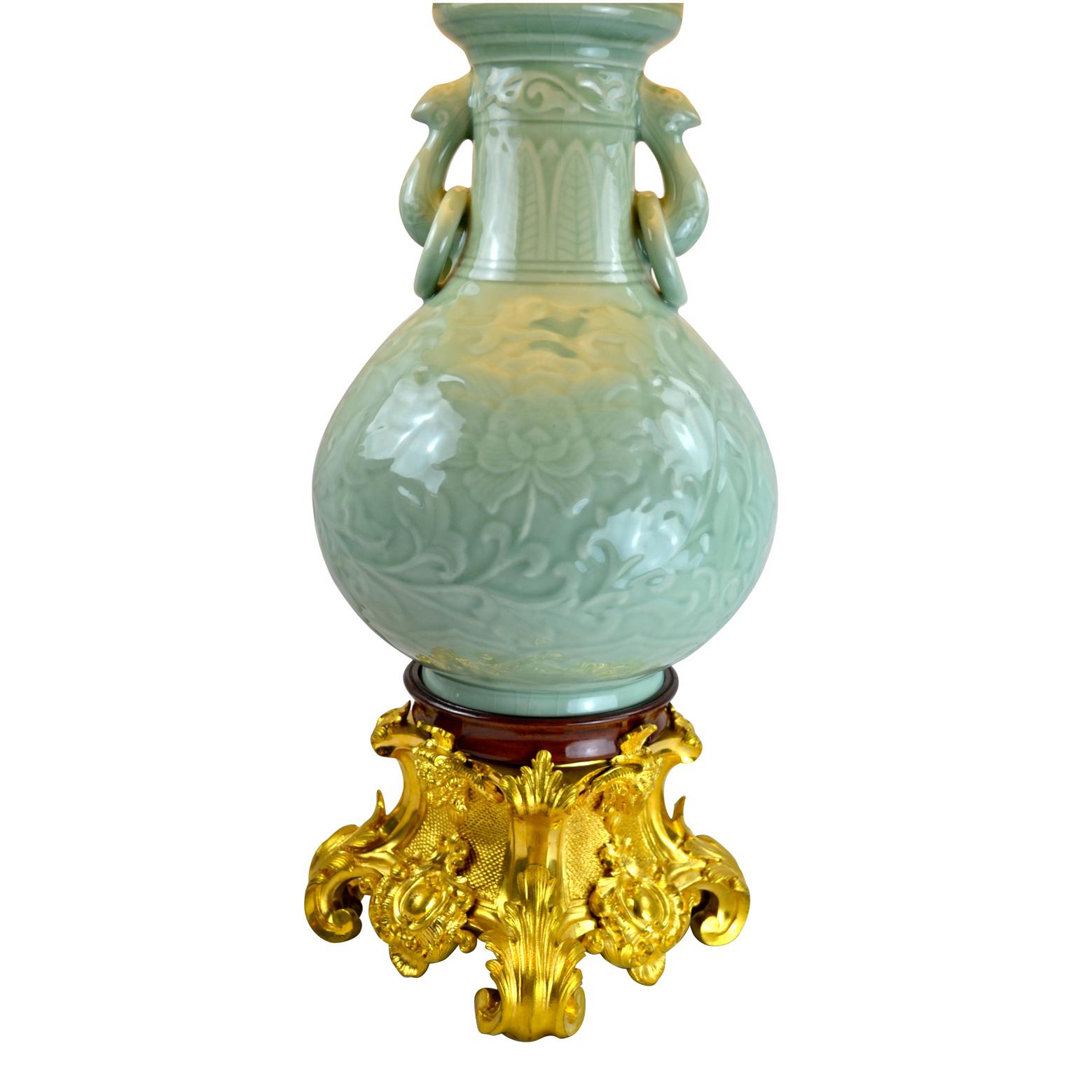 A Chinese celadon baluster vase lamp (likely 20th century porcelain) with loose ring handles on its neck. The vase is now set on a large scale finely chased and gilded bronze 19th century base of French origin.
  
 