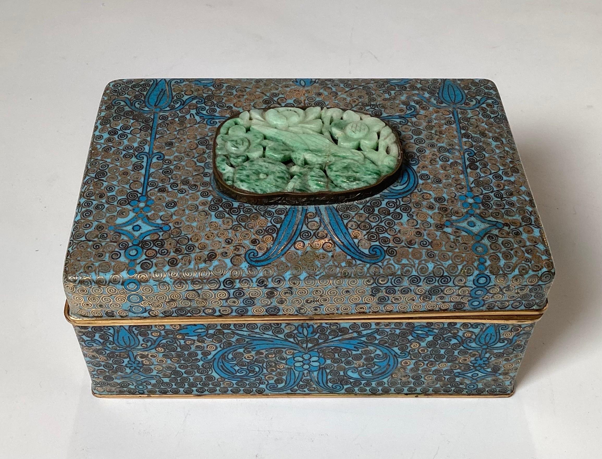 A diminutive Antique Chinese Cloisonné box with jade medallion line with wood. The enameled outside in shades of blue with gold color wiring with gilt at the edges, the interior is lined with a dark wood. 5 inches long, 3.5 inches deep, 2.5 inches