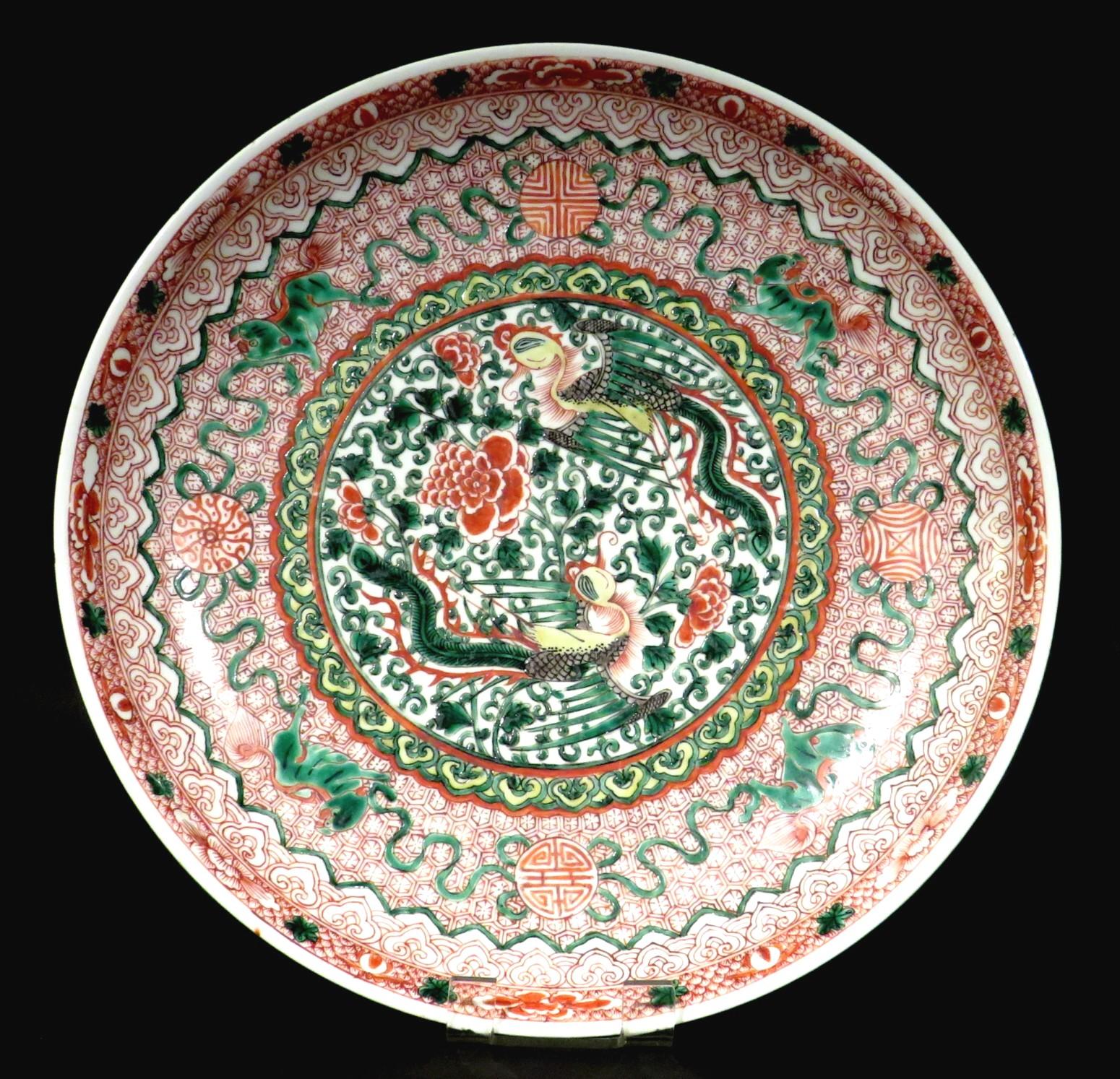Le champ central représente deux feng-huang (phénix) mythologiques entourant des fleurs de chrysanthème et des vignes à enroulement dans un bandeau de têtes de ruyi, le cavetto s'élevant sur un fond rouge fer de motifs de couches répétés,
