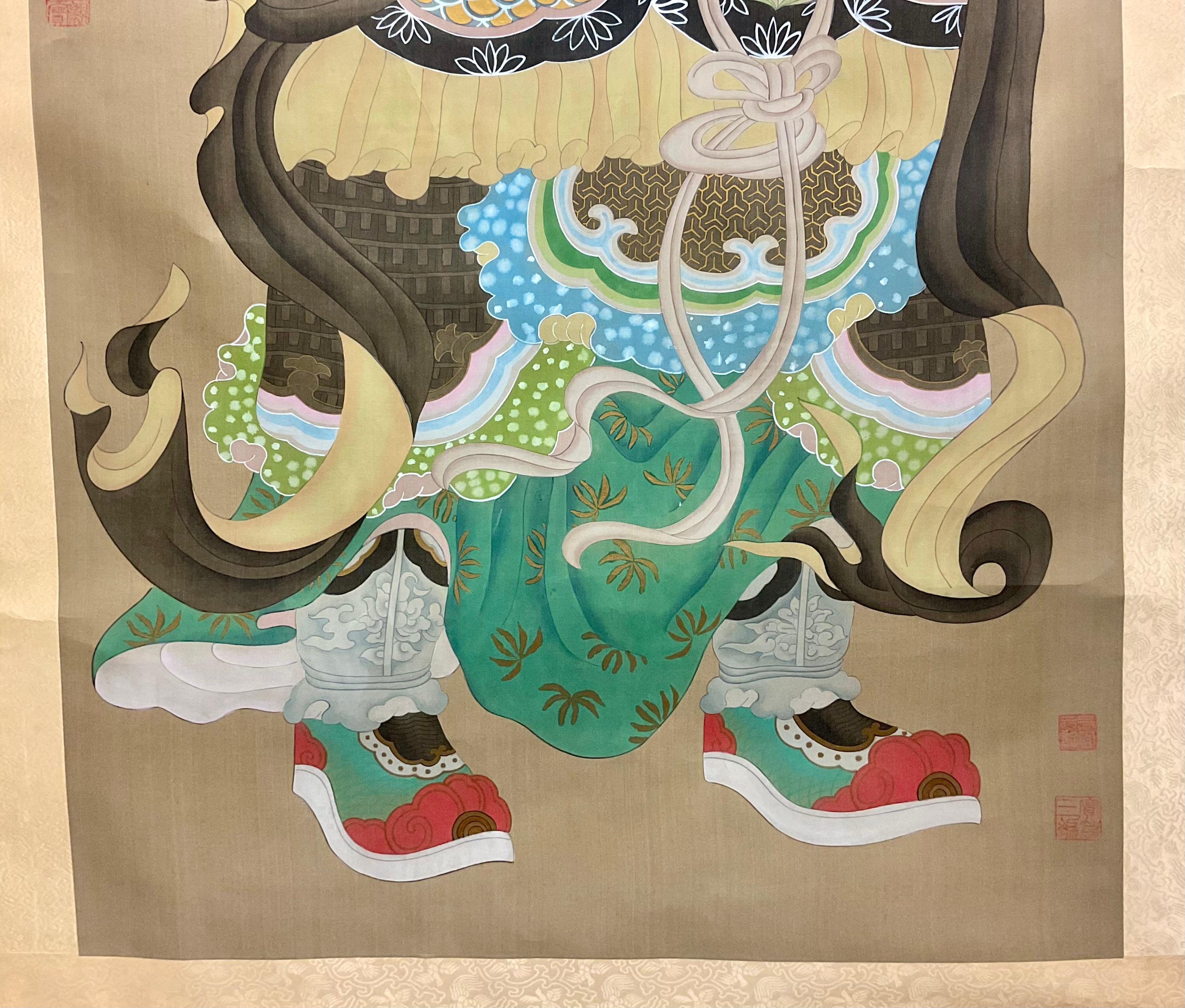 Antique framed Chinese scroll of an elder Chinese man. Scroll features a bearded Chinese man wearing traditional colorful and ornate clothing. Vibrant colors of teal, red, gold and brown on a tan background. Framed in a carved wooden frame with gold