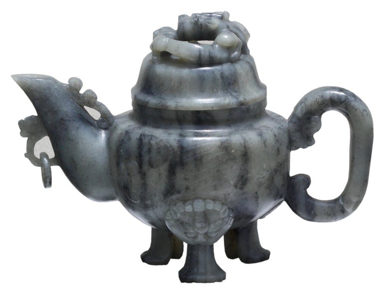 A Chinese jade teapot and cover 
of variegated grey and black color, the surface highly polished and carved in very low relief on one side with a prunus tree and rockwork, and on the other with rocky outcrop, set with a chilong-form handle and