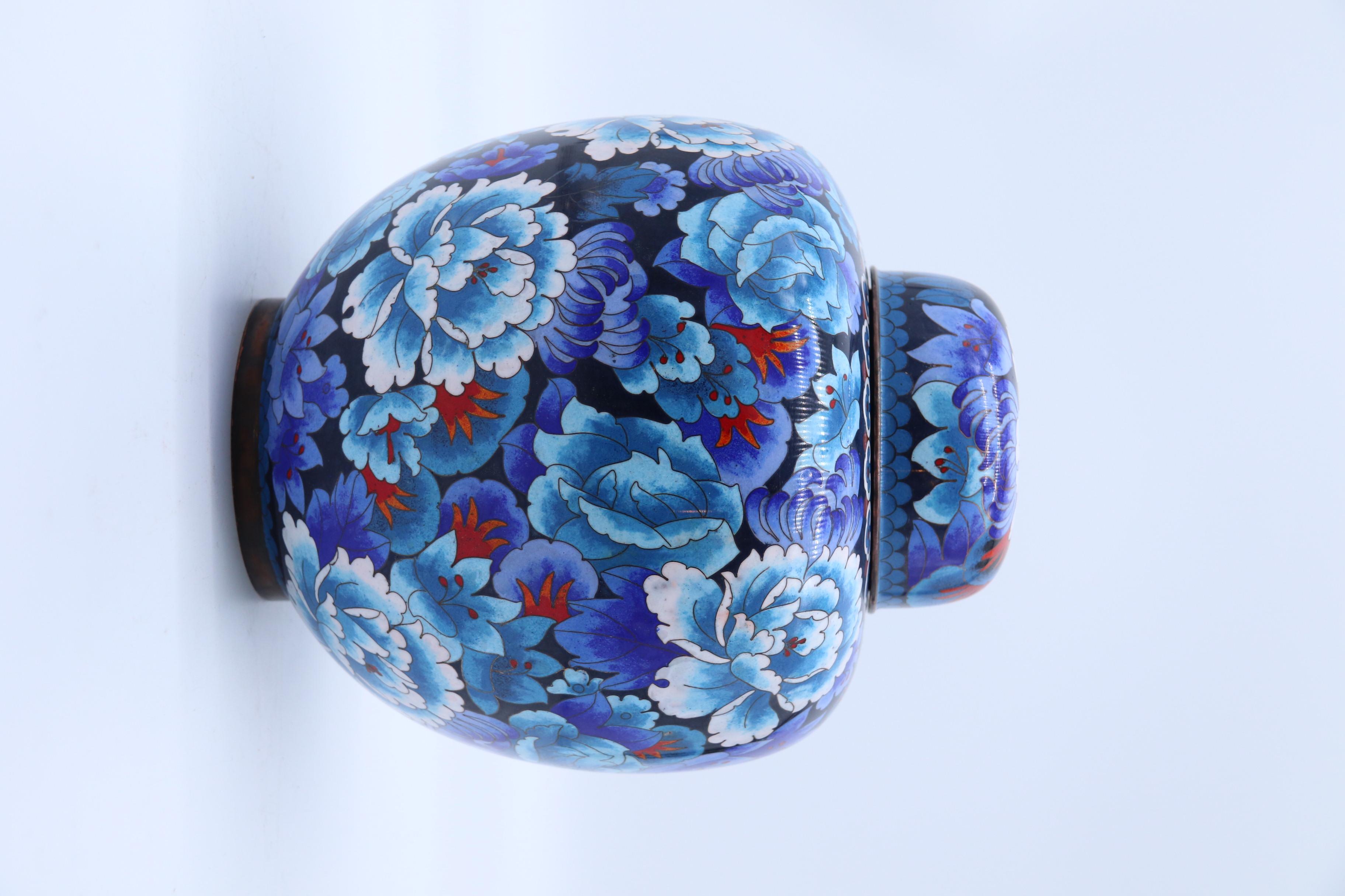 This most eye catching fine large cloisonné lidded ginger jar dates to the mid 20th century and is a true work of art. It is completely covered in a multitude of exotic flowers mainly peonies in rich vibrant colours over a dark ground. The