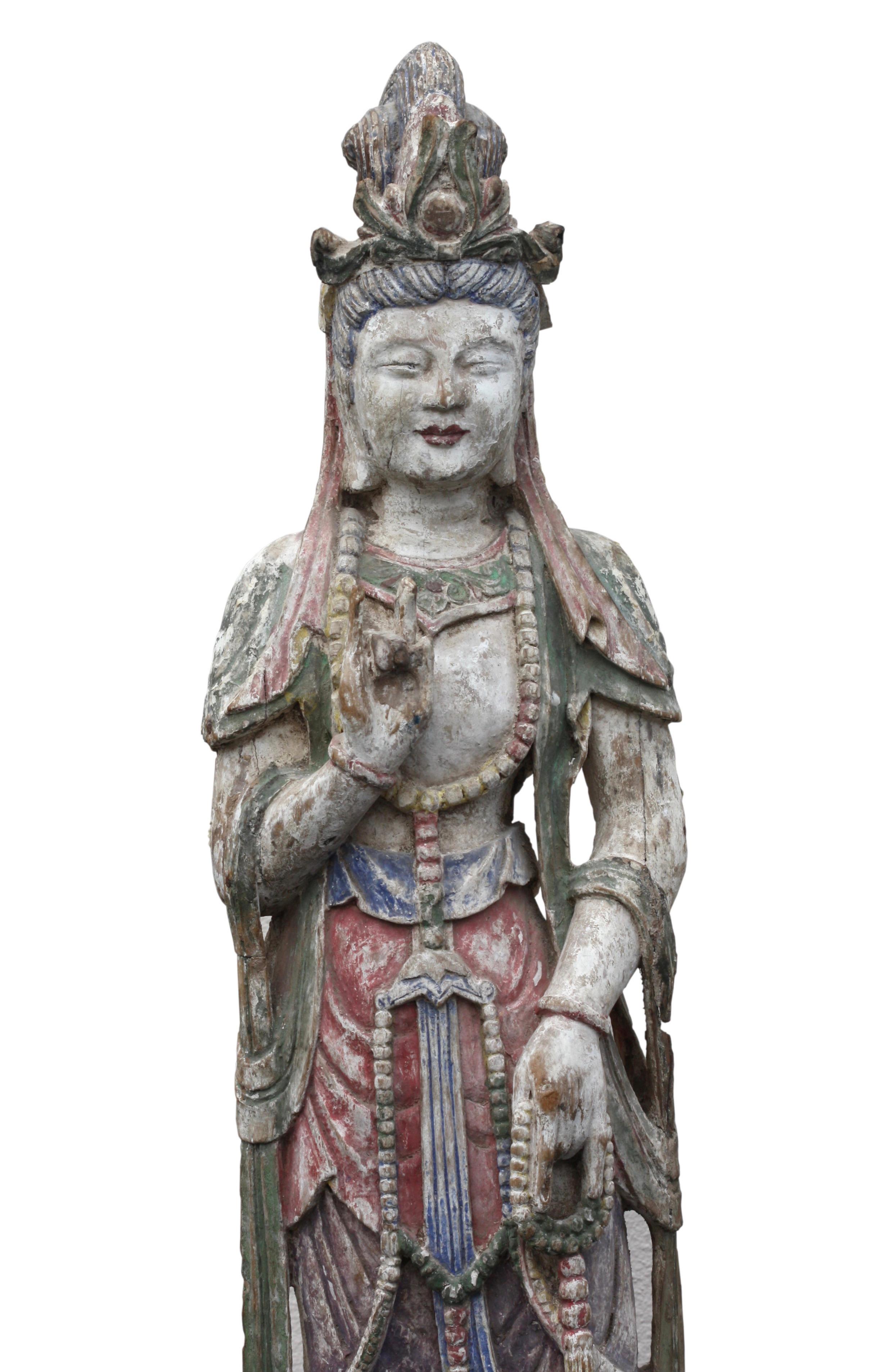 Figure chinoise en bois sculpté et décoré de polychromes représentant un Bodhisattva
Debout, les mains en vitarka mudra, la tête ornée d'un diadème à cinq branches, le visage anguleux avec un nez large et plat et des lèvres proéminentes, les