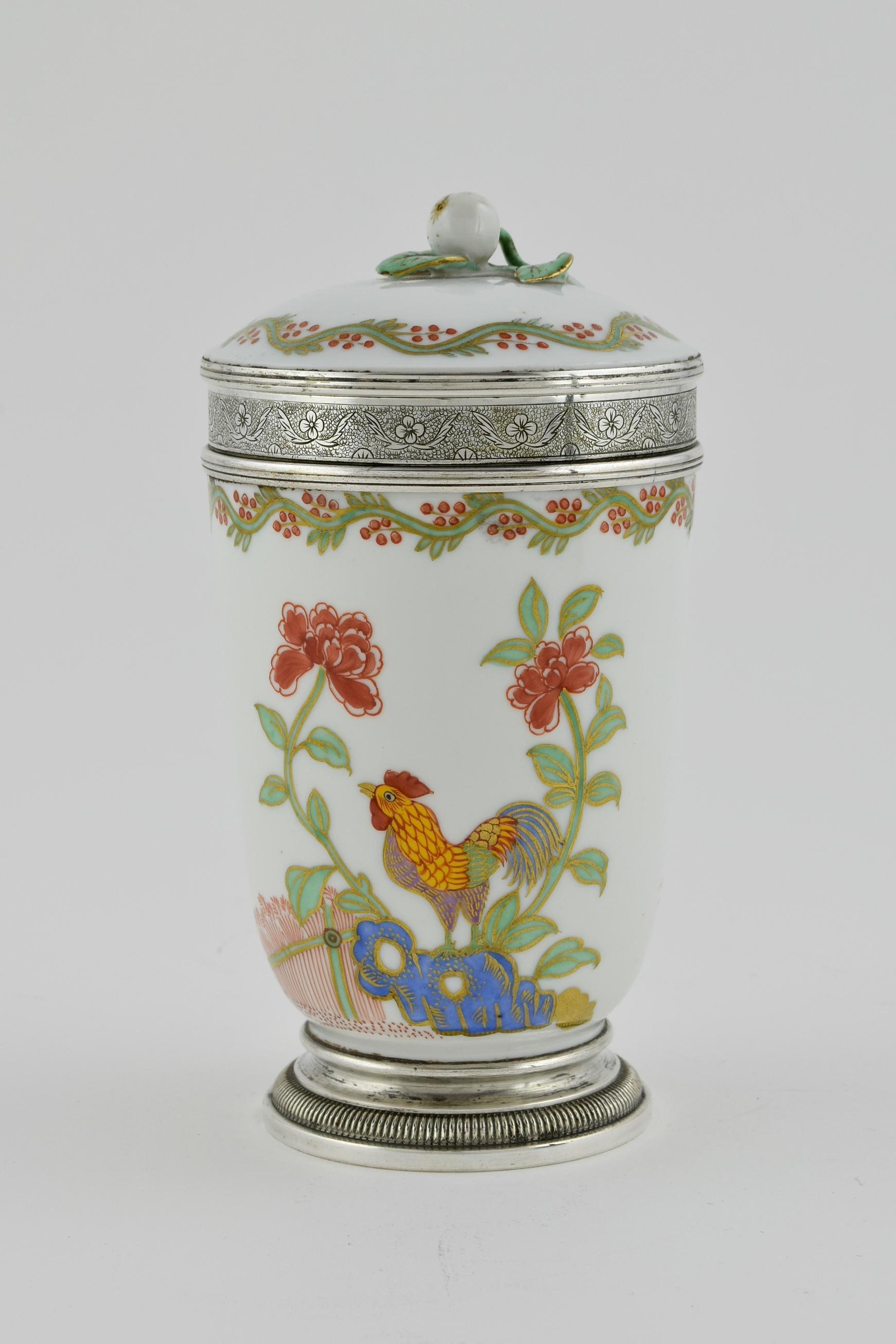 This cup and cover displays figures in traditional dress, interacting on one side, and on the other a cockerel. The body and lid of the cup is beautifully decorated with ascetically pleasing flowers, foliage and birds. The finial is formed as a
