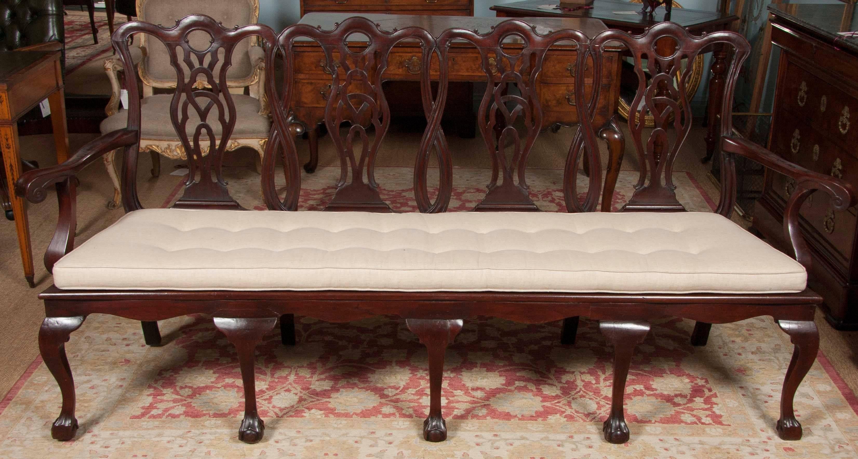 A 19th century mahogany four-seat settee with a carved open back and caned seat. The arms are shaped with scroll ends and the seat frame is mounted on cabriole legs with ball and claw feet. The cushion is later.