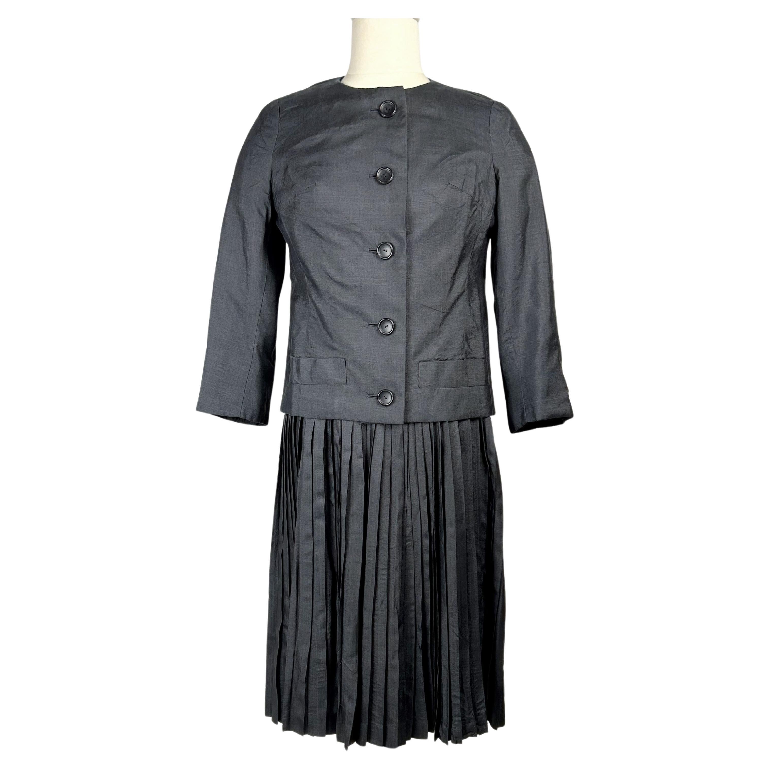 Vers 1958-1960

États-Unis

Élégant tailleur habillé en tissu de soie gris anthracite sous licence américaine de la maison Christian Dior, datant probablement des années Yves Mathieu Saint-Laurent. Robe à col ras du cou avec buste ajusté, manches