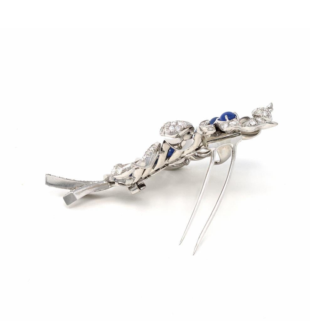The exquisite brooch circa 1950 represents a skillfully designed feather featuring a line of perfectly matched medium blue star sapphires on the shaft with diamonds set at the extremities of each barb and mix cut diamonds at the bottom. The cabochon